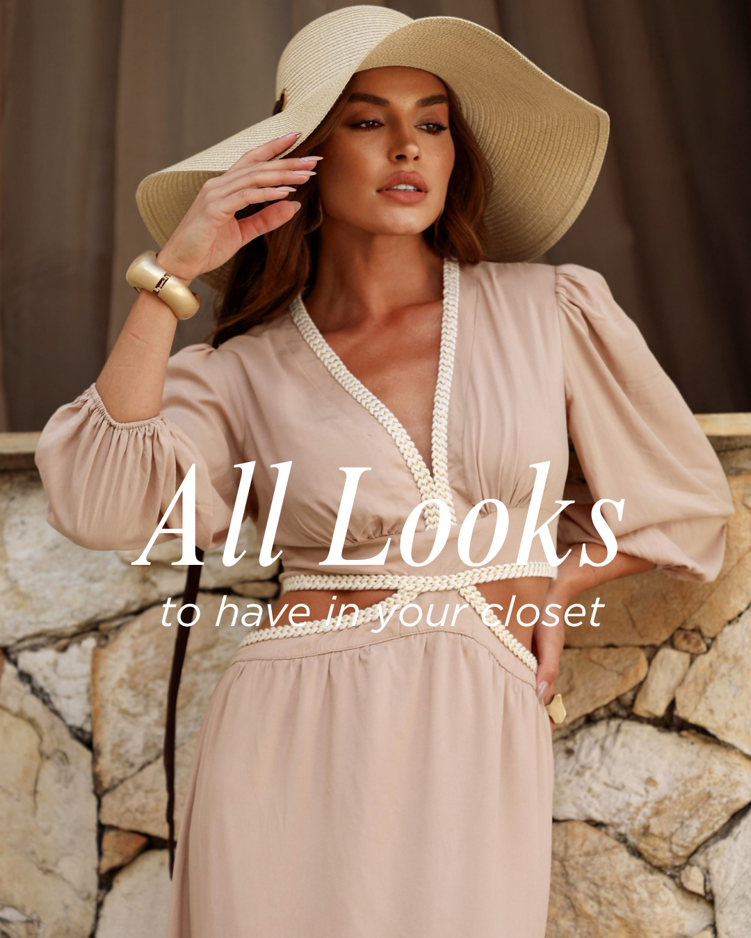 Mulher usando chapéu de palha amplo, vestido bege de manga longa com detalhes em corda, diante de parede de pedra, promovendo moda feminina e acessórios.