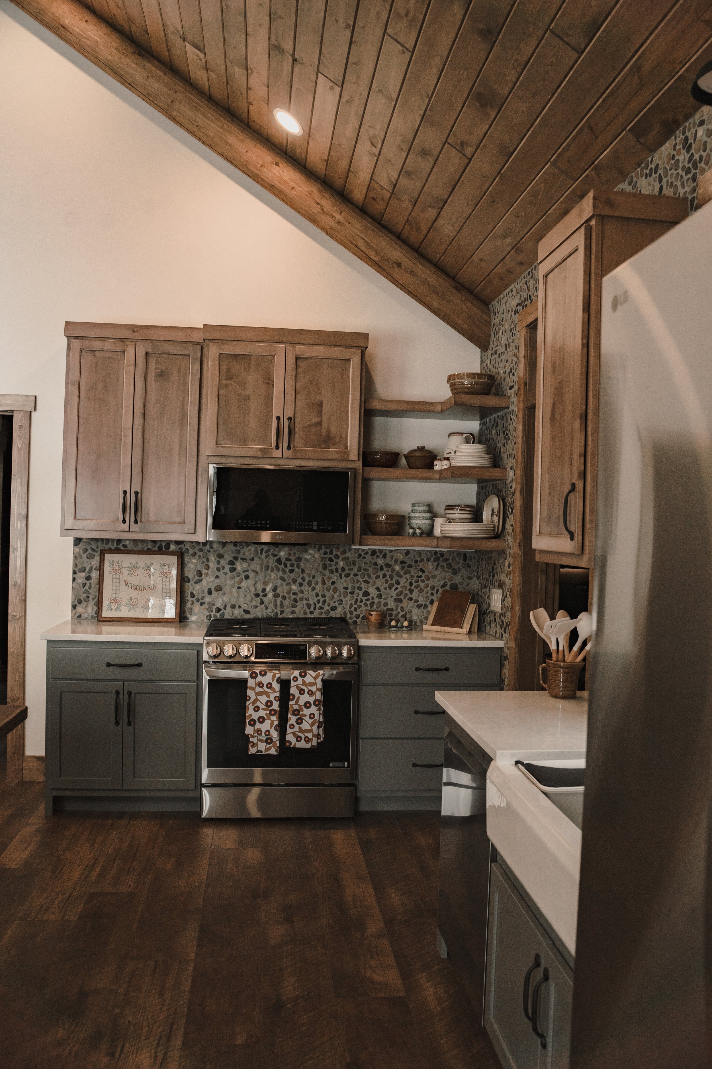 Custom kitchen with wood cabinetry, open shelving, tiled backsplash and large cooking range.