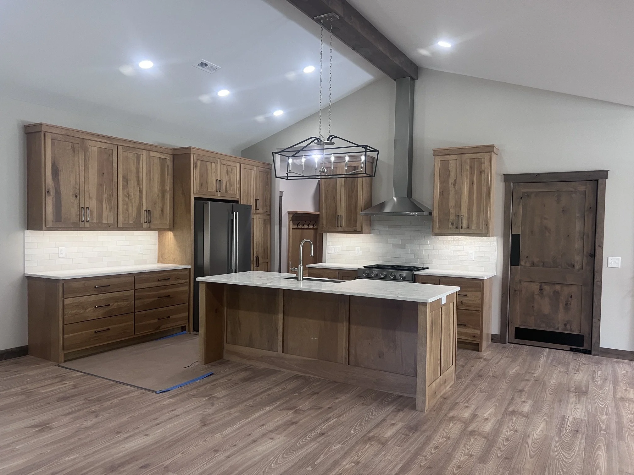 Custom kitchen with natural wood cabinetry, large center island, pendant lighting and matching wood barn door.