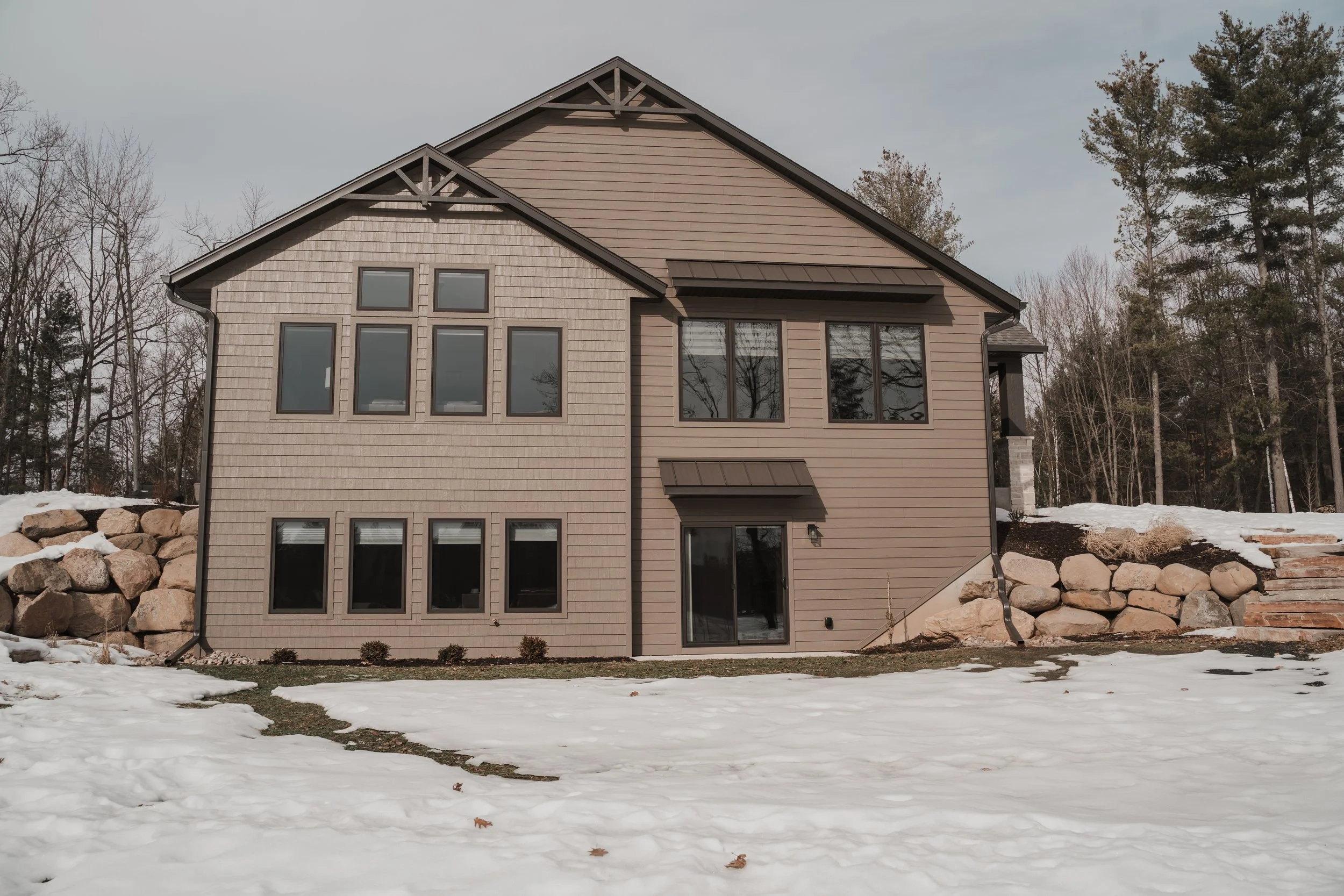 Newly constructed home exterior with mixed siding, stone accents, large windows and covered entry.