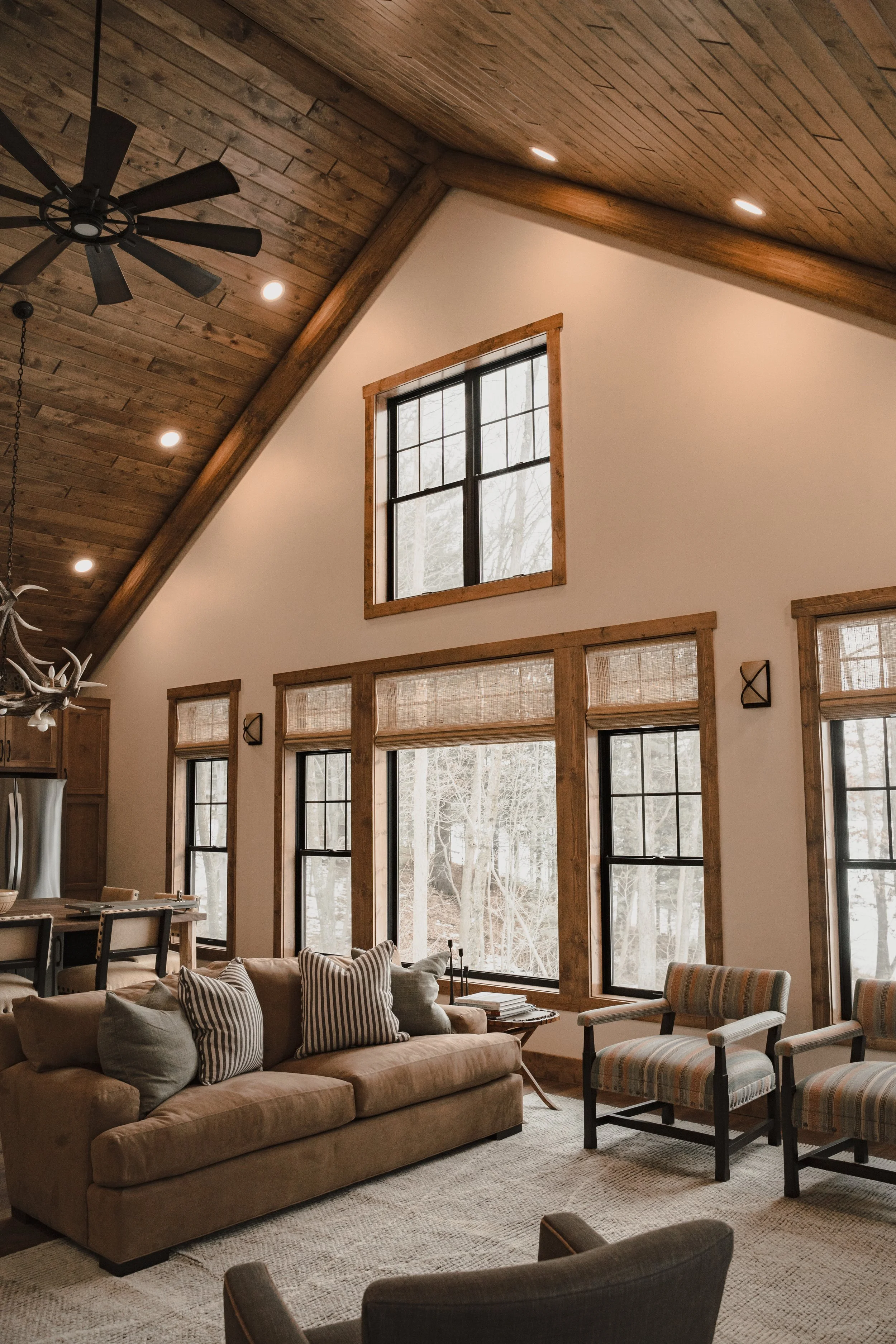 Open living room with vaulted wood ceiling, large windows, wood trim and natural light.