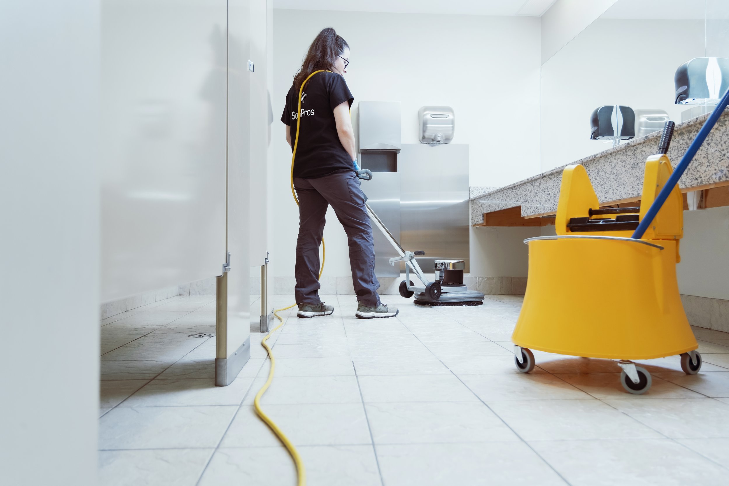 Woman in SanPros shirt washing office bathroom floor