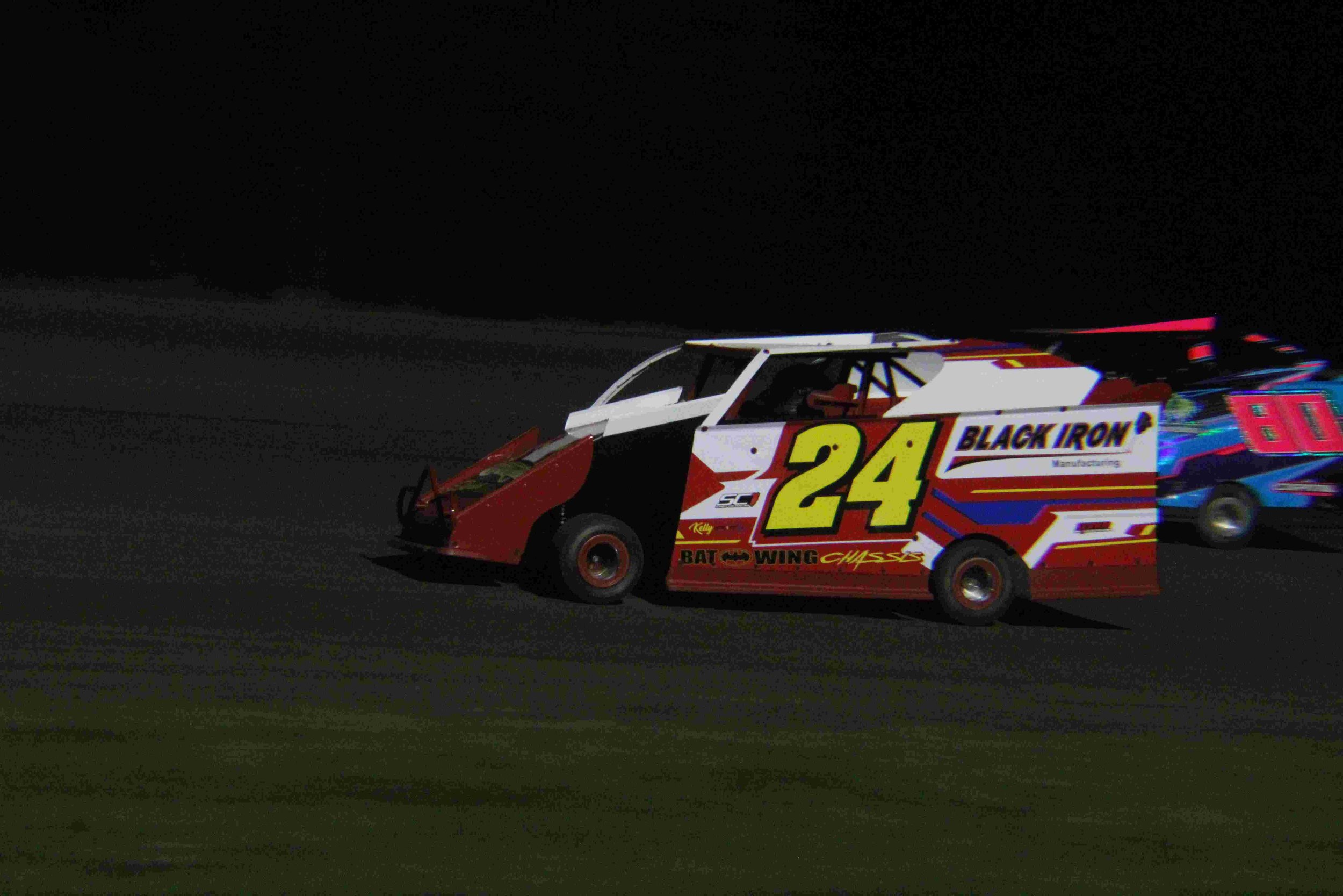 Race car number 24 driving on a dirt track at night