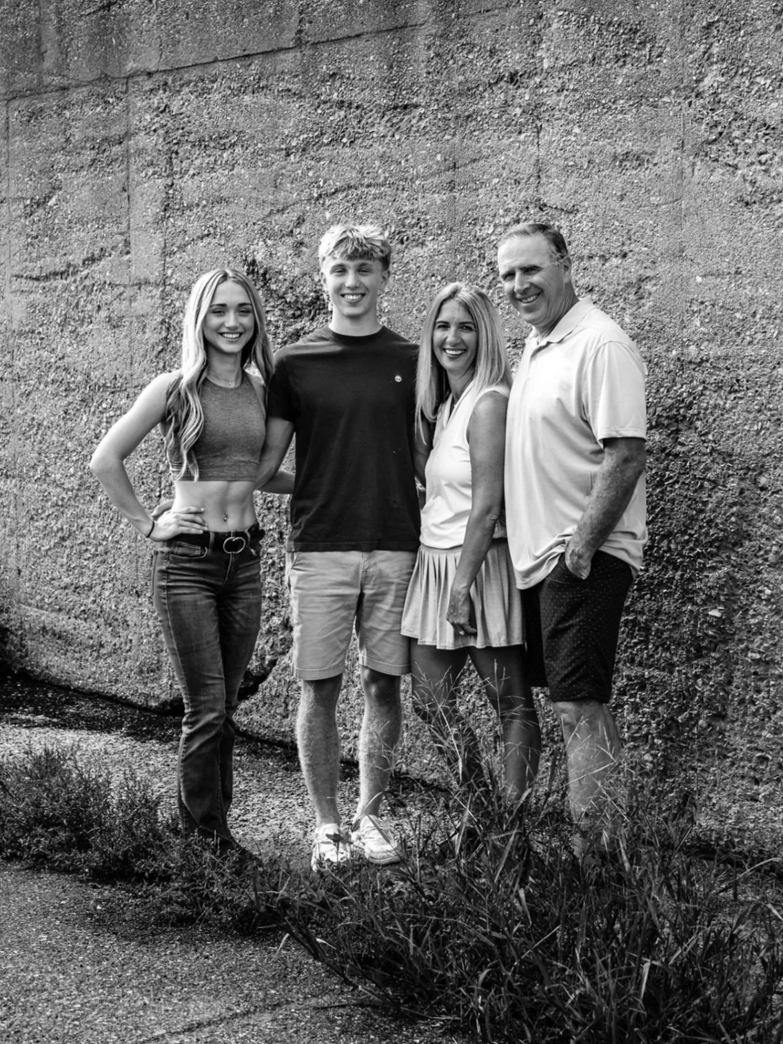 A black and white photo of four people standing in front of a textured wall, smiling for the camera.
