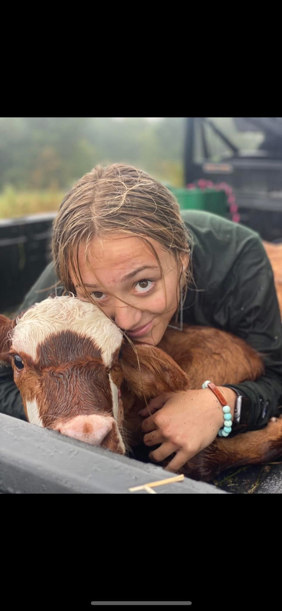 A young woman with wet hair hugging a calf with light brown and white spots.