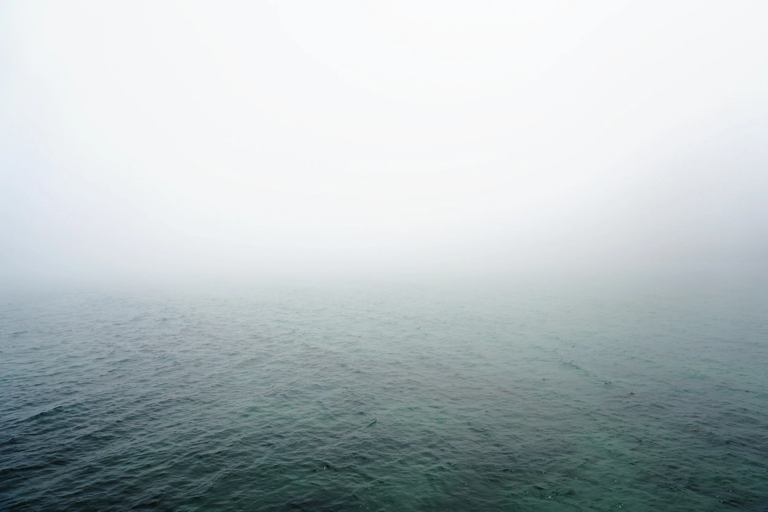 Image of a vast ocean or sea with calm waters and foggy, overcast sky.