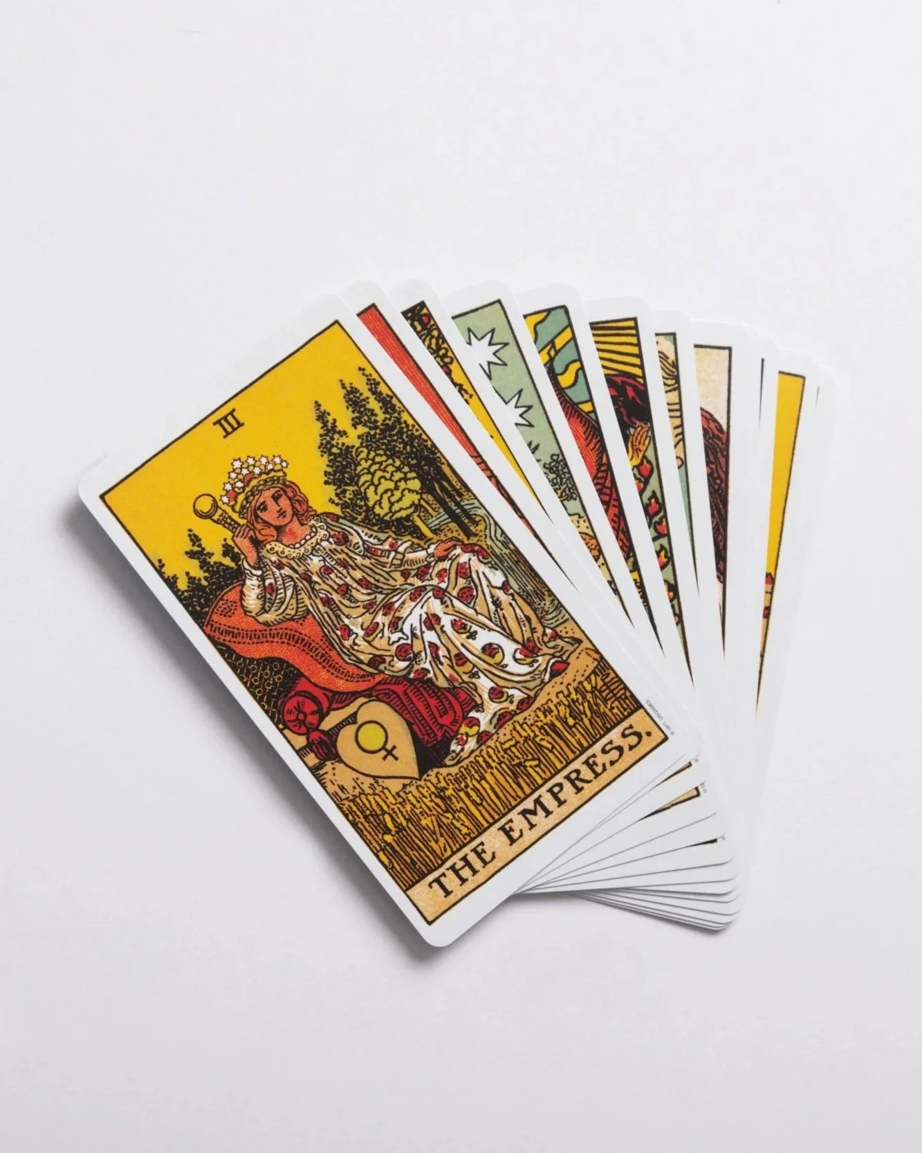 A spread of tarot cards with the Empress card at the front, showing a woman sitting on a throne with a crown of stars, holding a scepter, with trees behind her.