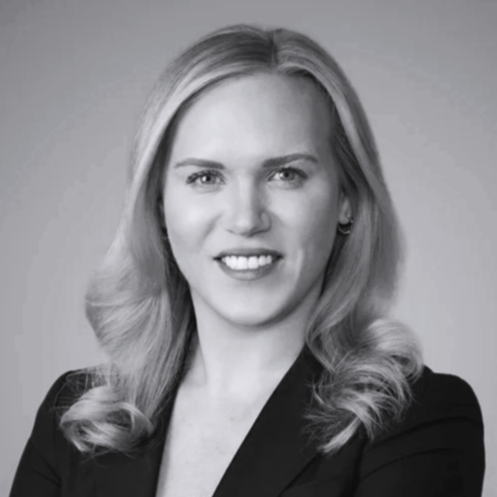 Black and white professional portrait of a woman with wavy blonde hair, wearing a blazer, smiling at the camera.