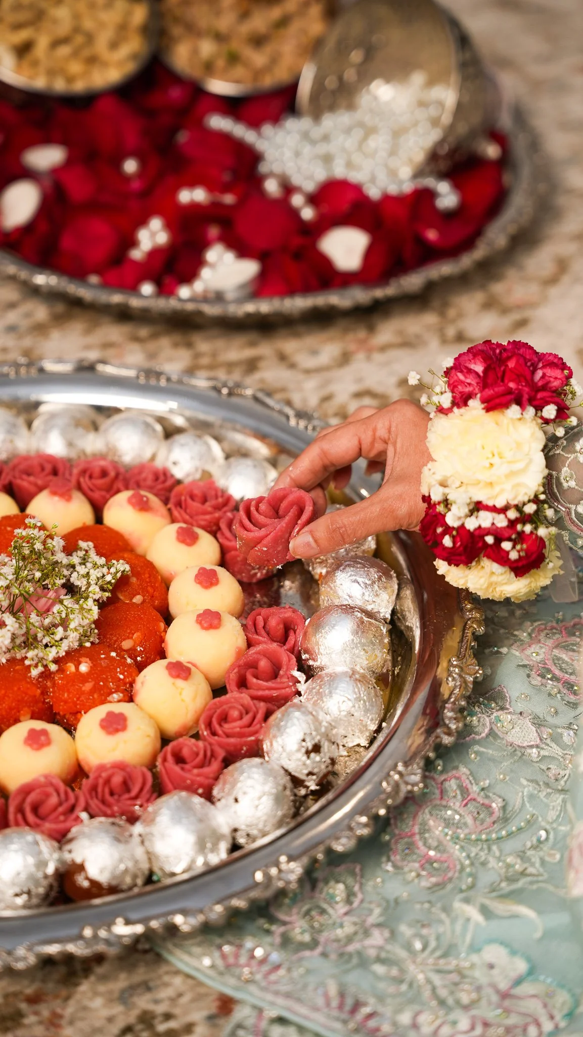 A tray of assorted wedding desserts decorated with small flower designs and a person's hand placing a pink flower-shaped treat.