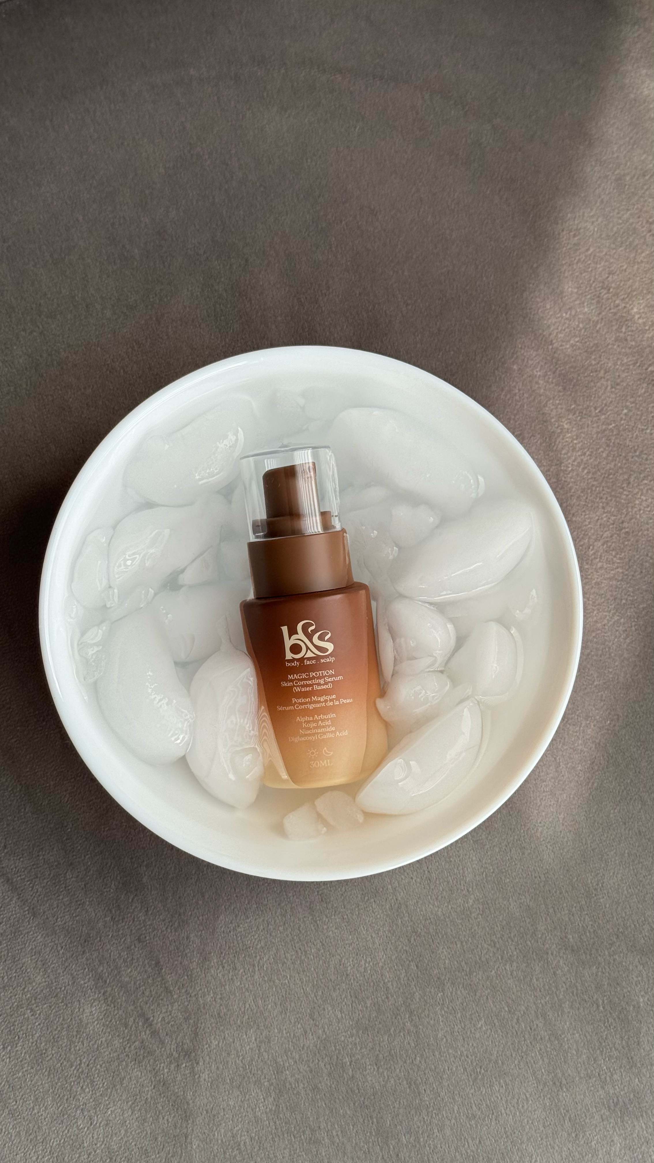 A small brown spray bottle labeled 'b&s body, face, scalp' placed in a white bowl filled with ice cubes.