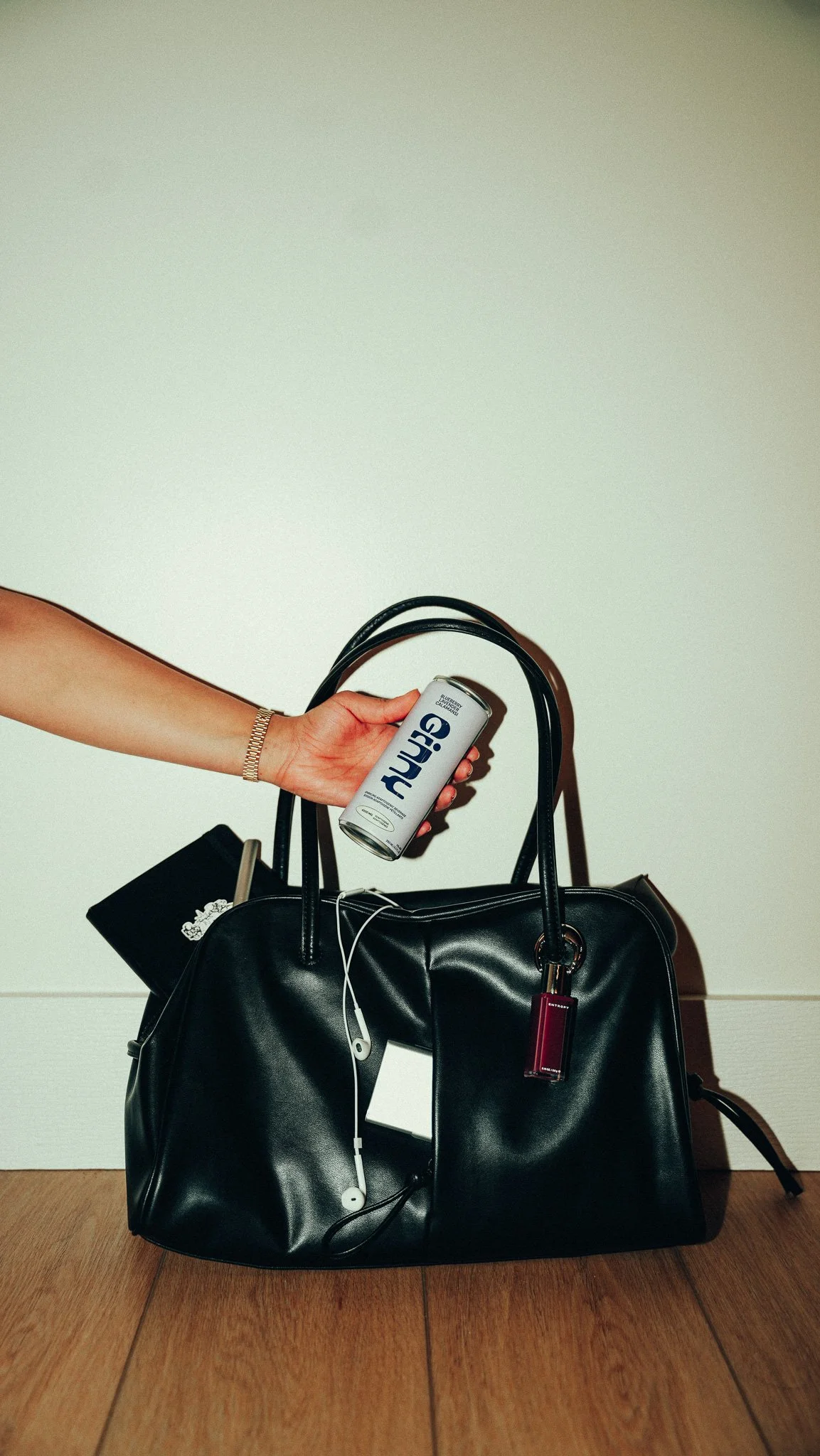 A person holding a can of sparkling water over a black handbag with a white background.