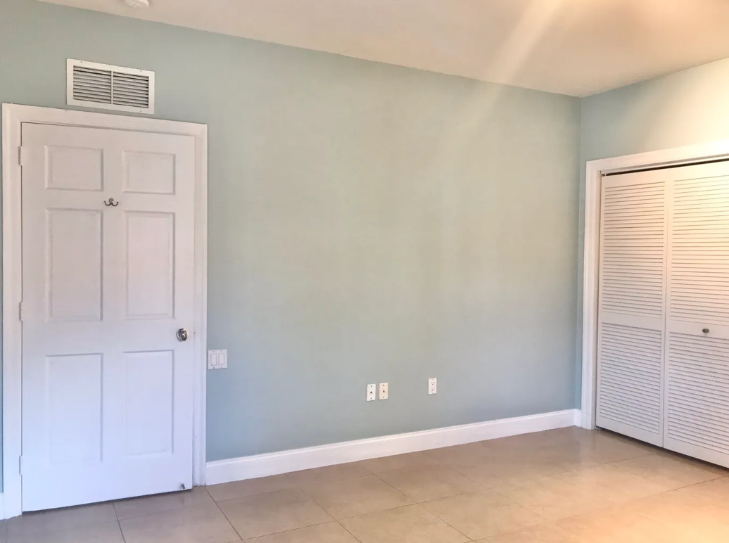 Empty room with light green walls, white door, closet with louvered doors, ceramic tile floor, and ceiling vent.