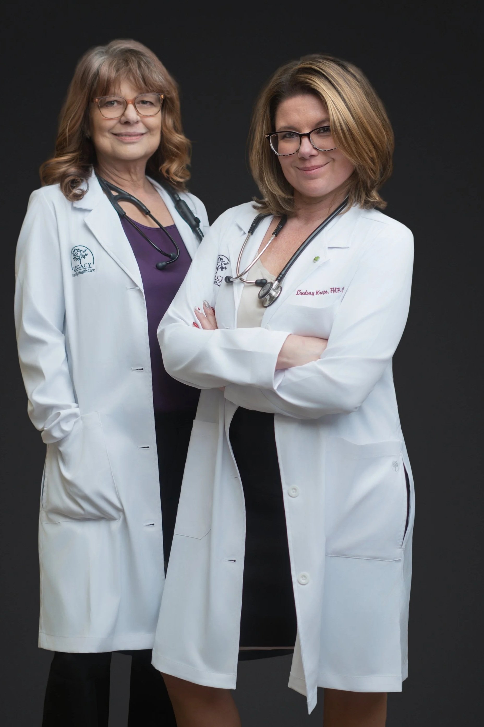 A female doctor with glasses, brown hair, wearing a white coat and stethoscope around her neck, smiling.