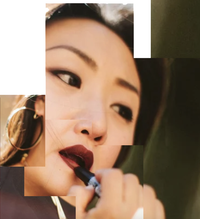 Close-up of a woman applying dark lipstick with her finger, wearing gold hoop earrings, with makeup and dark hair.