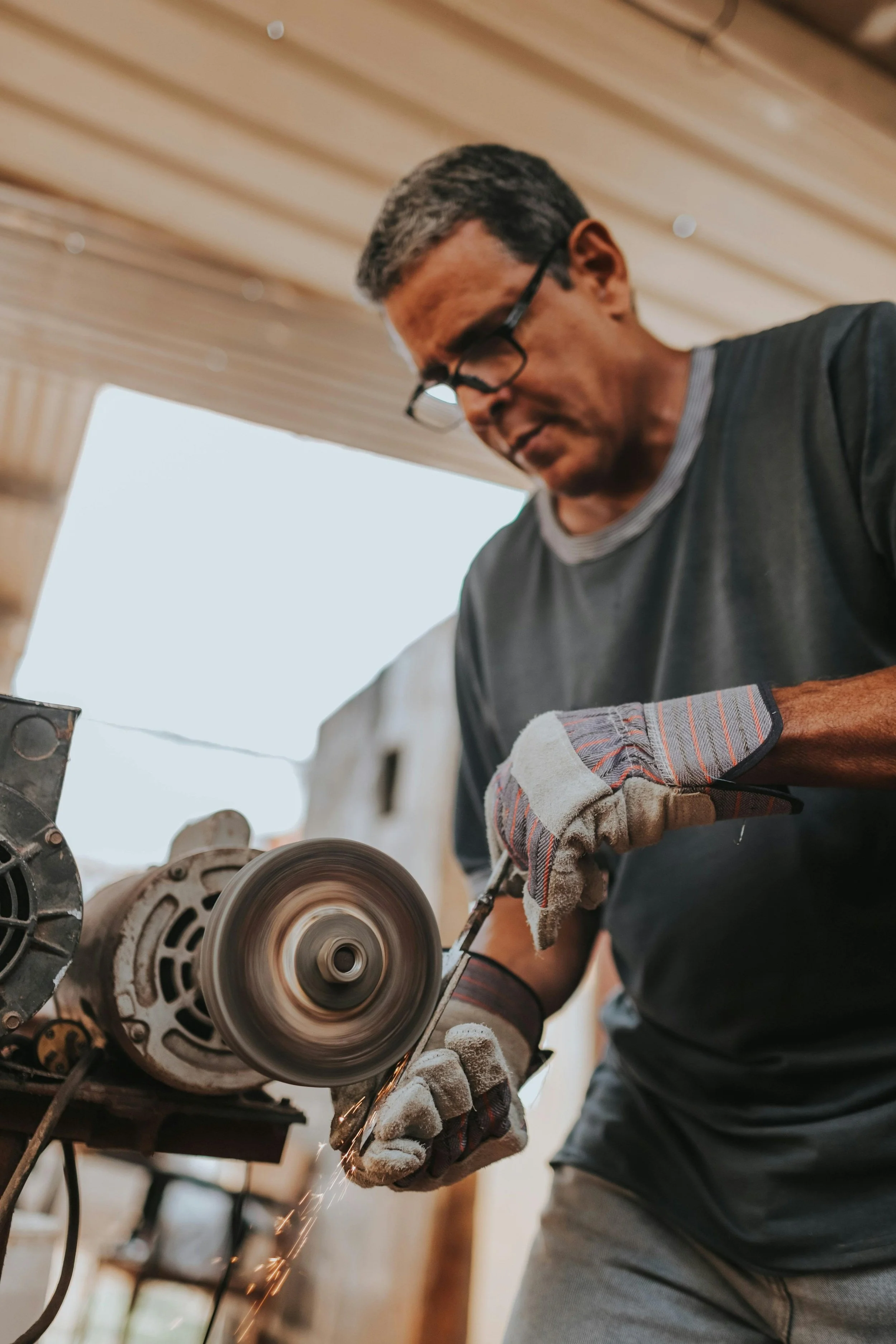 A man wearing glasses and gloves is using a power tool to cut metal in a workshop.