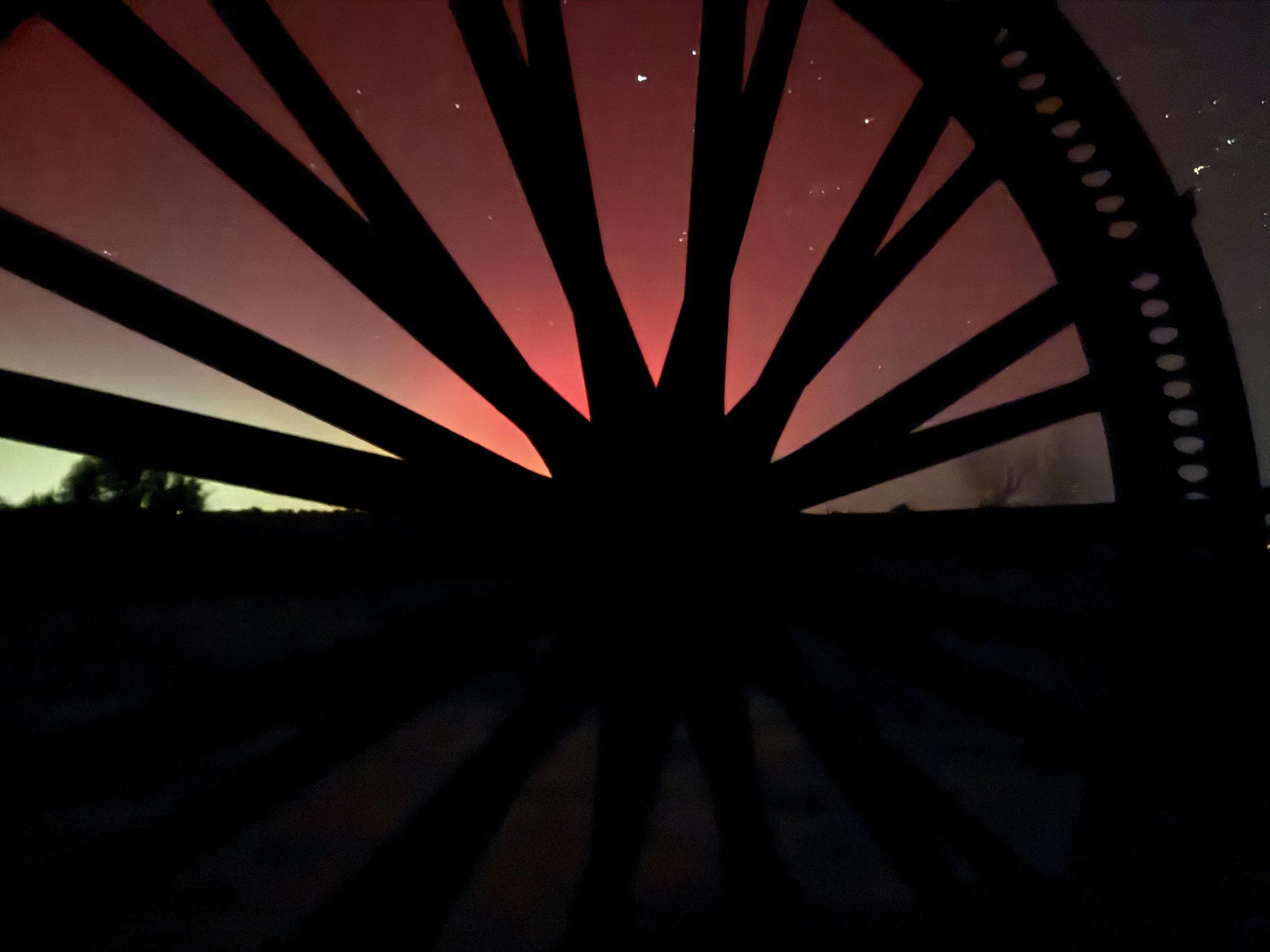 Northern lights behind rustic wagon wheel at Lost Pond wedding venue in Penrose Colorado