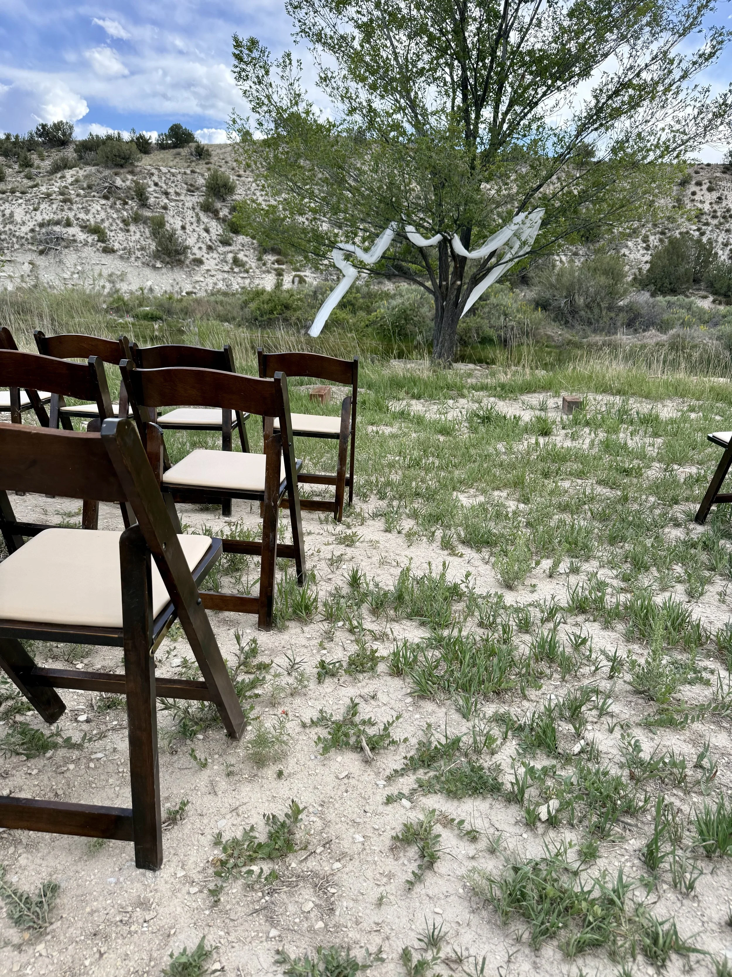 Pondside outdoor wedding ceremony with wooden garden chairs and arbor under the elm, for a garden wedding ceremony and wedding venue near Pueblo, Colorado.