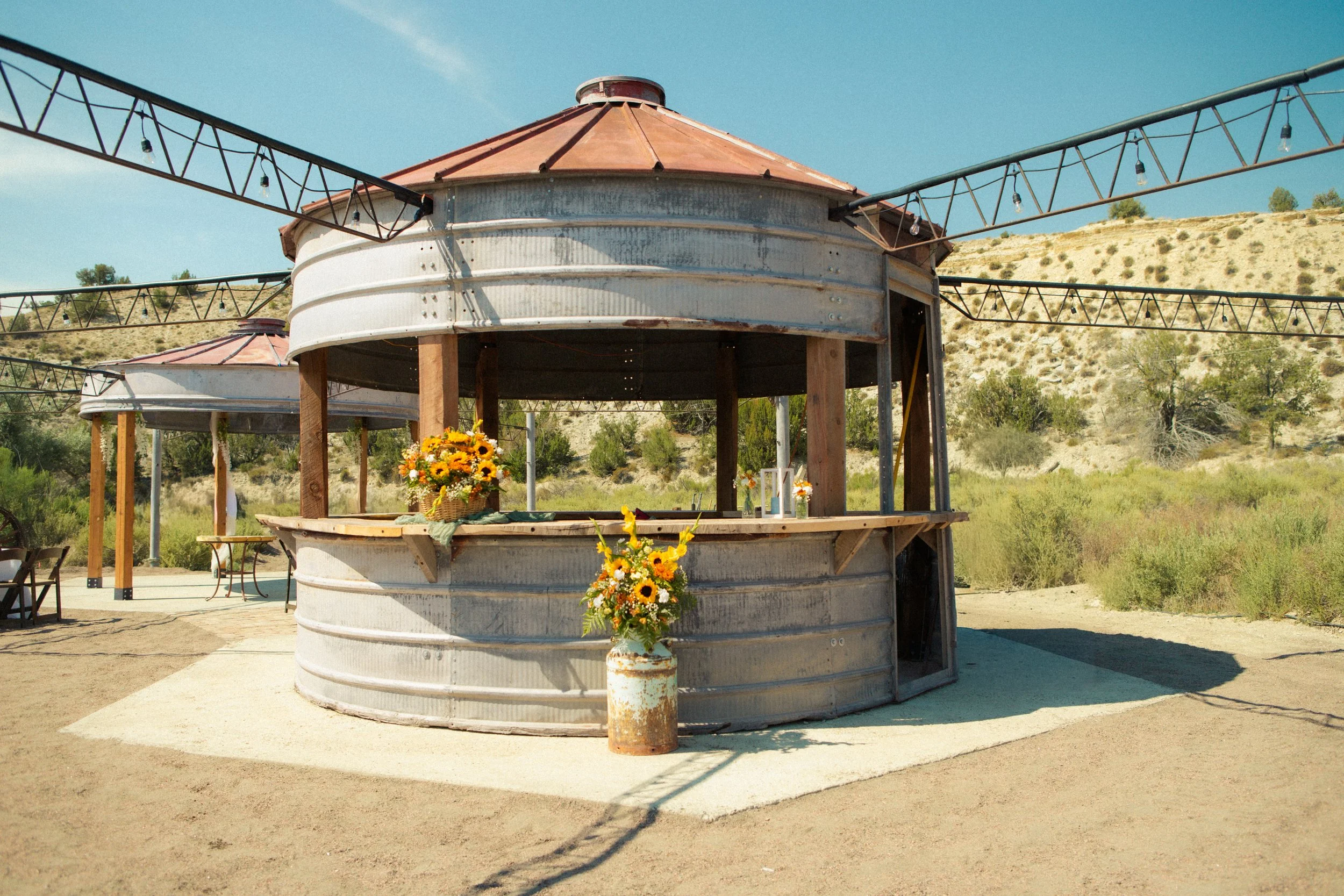 Rustic 360 degree Silo Bar under the string lights by the water at outdoor wedding venue Lost Pond near Canon City, Colorado.