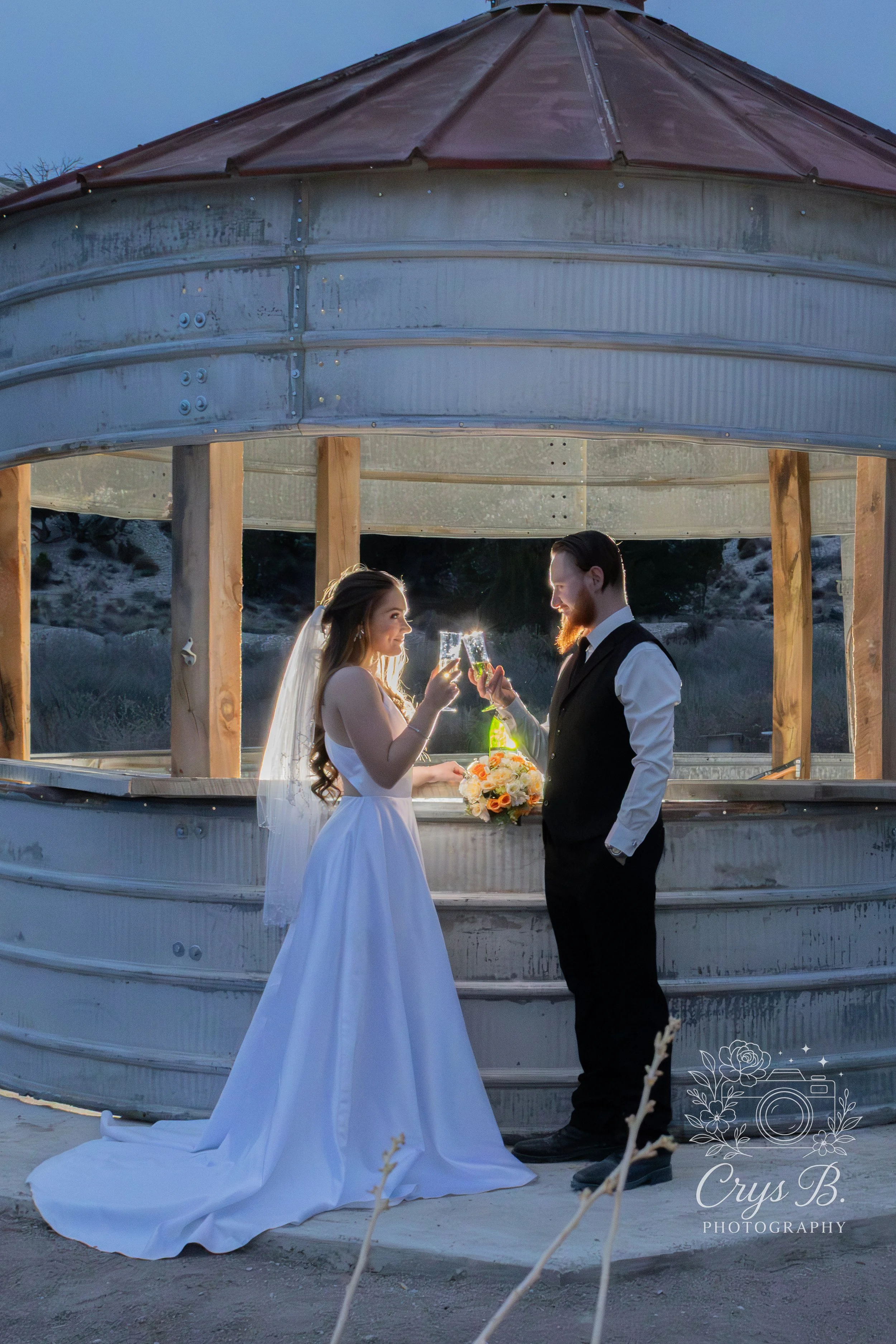 Bride and groom making champagne toast by the silo grain bin bar at Lost Pond wedding venue, a waterfront wedding venue with natural water features near Pueblo, Colorado