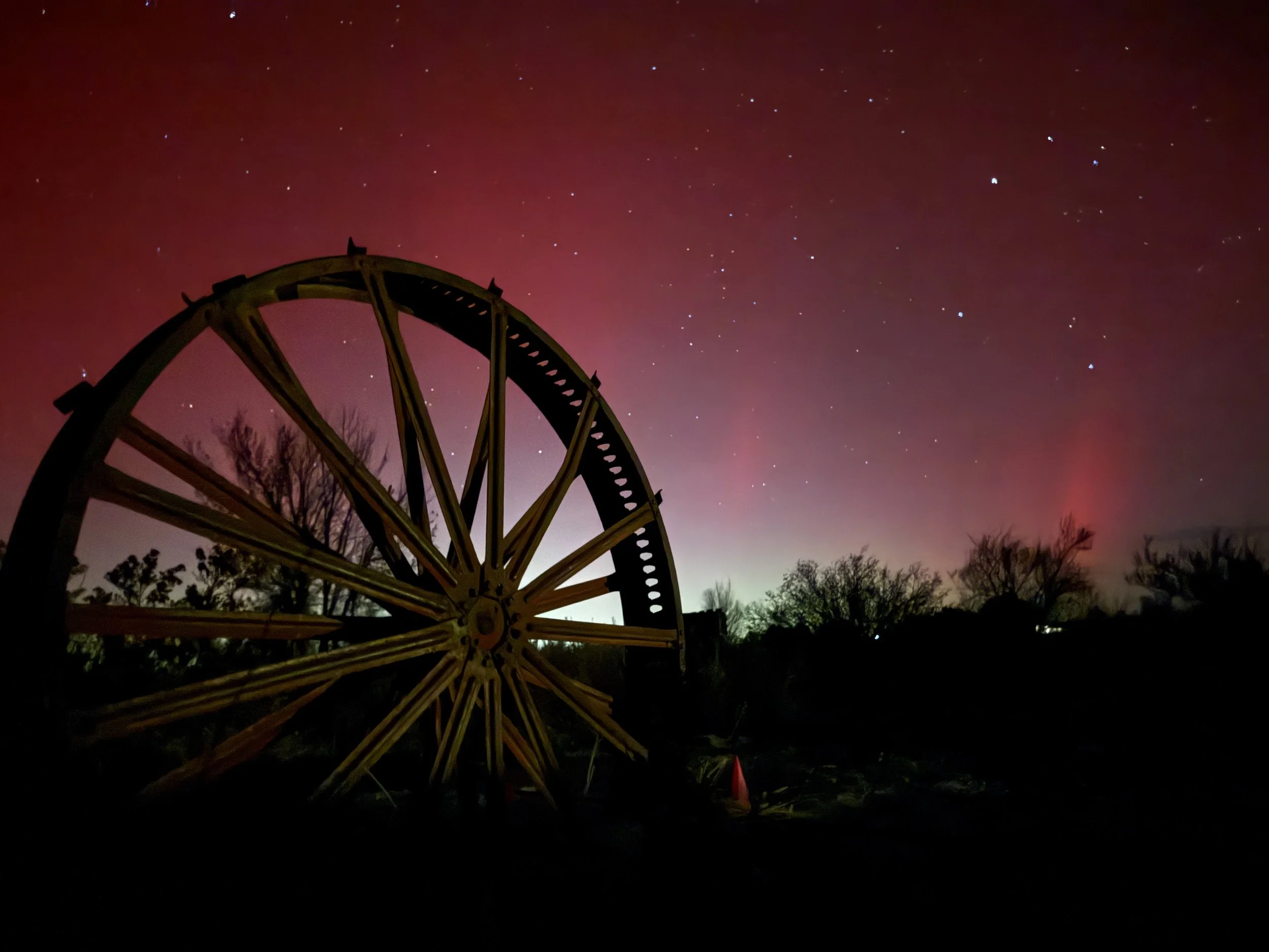 Northern lights behind rustic wagon wheel at Lost Pond wedding venue near Canon City Colorado