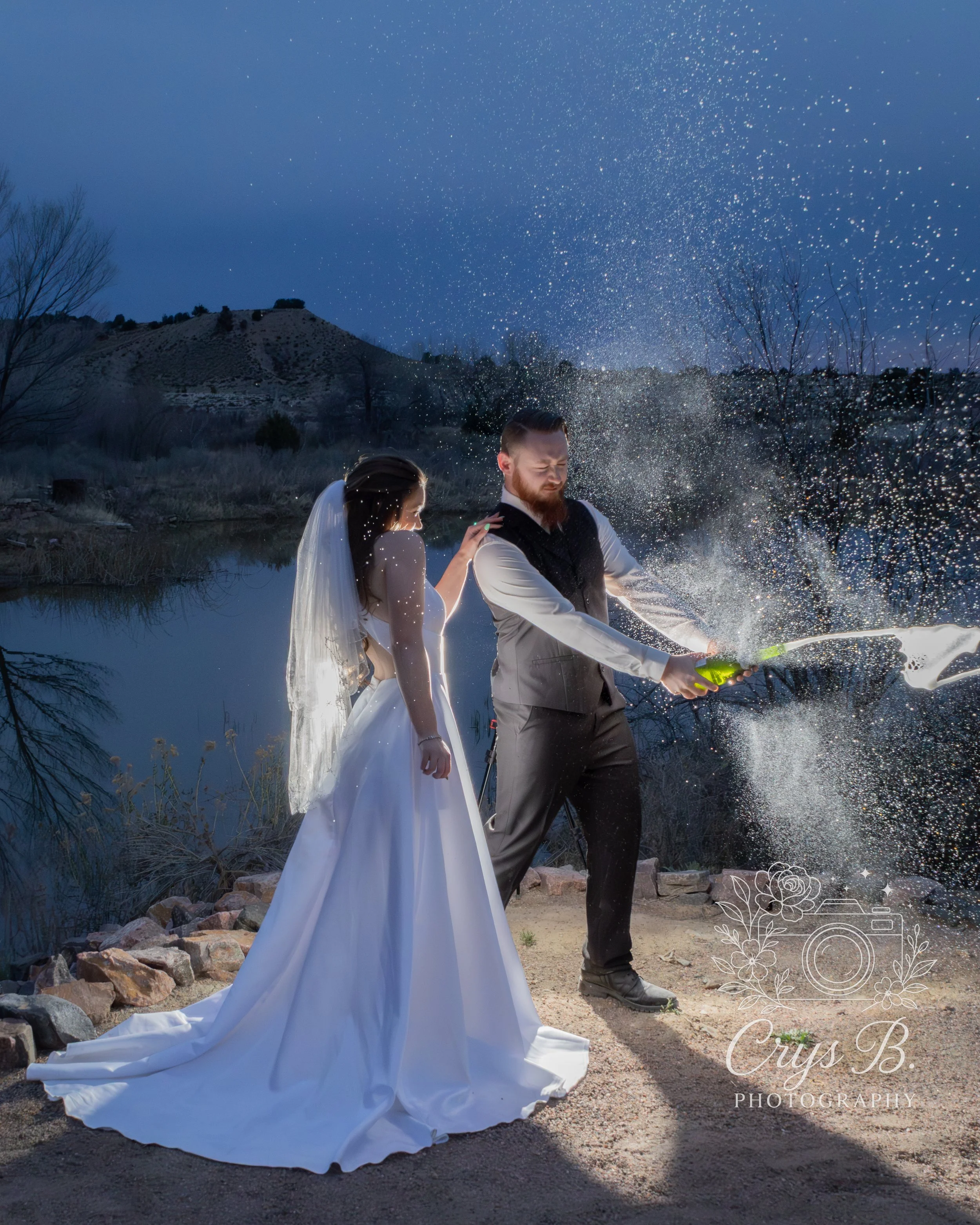 Bride and groom pop champaign next to the pond during the wedding reception at their wedding celebration at Lost Pond wedding venue near Canon City, Colorado.