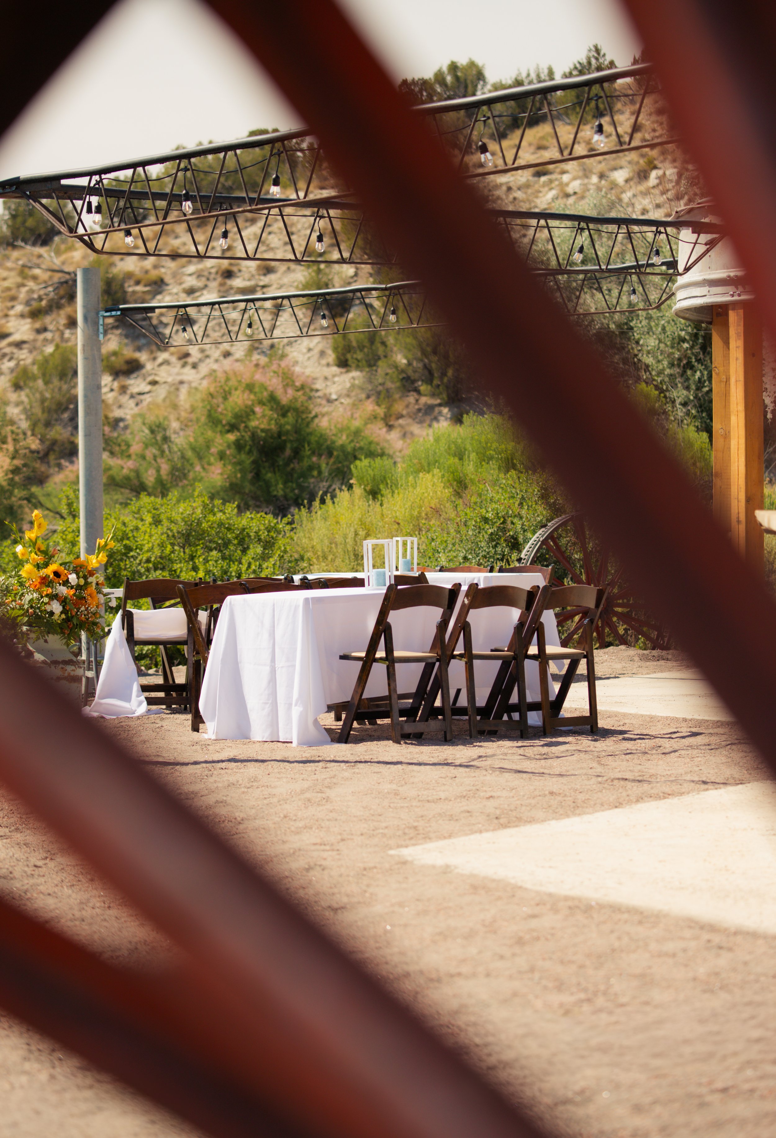 Beautiful wedding reception table setting are set up at Lost Pond wedding venue, an outdoor wedding venue near Colorado Springs, Pueblo, and Canon City, Colorado. Picture taken through rustic wagon wheel.