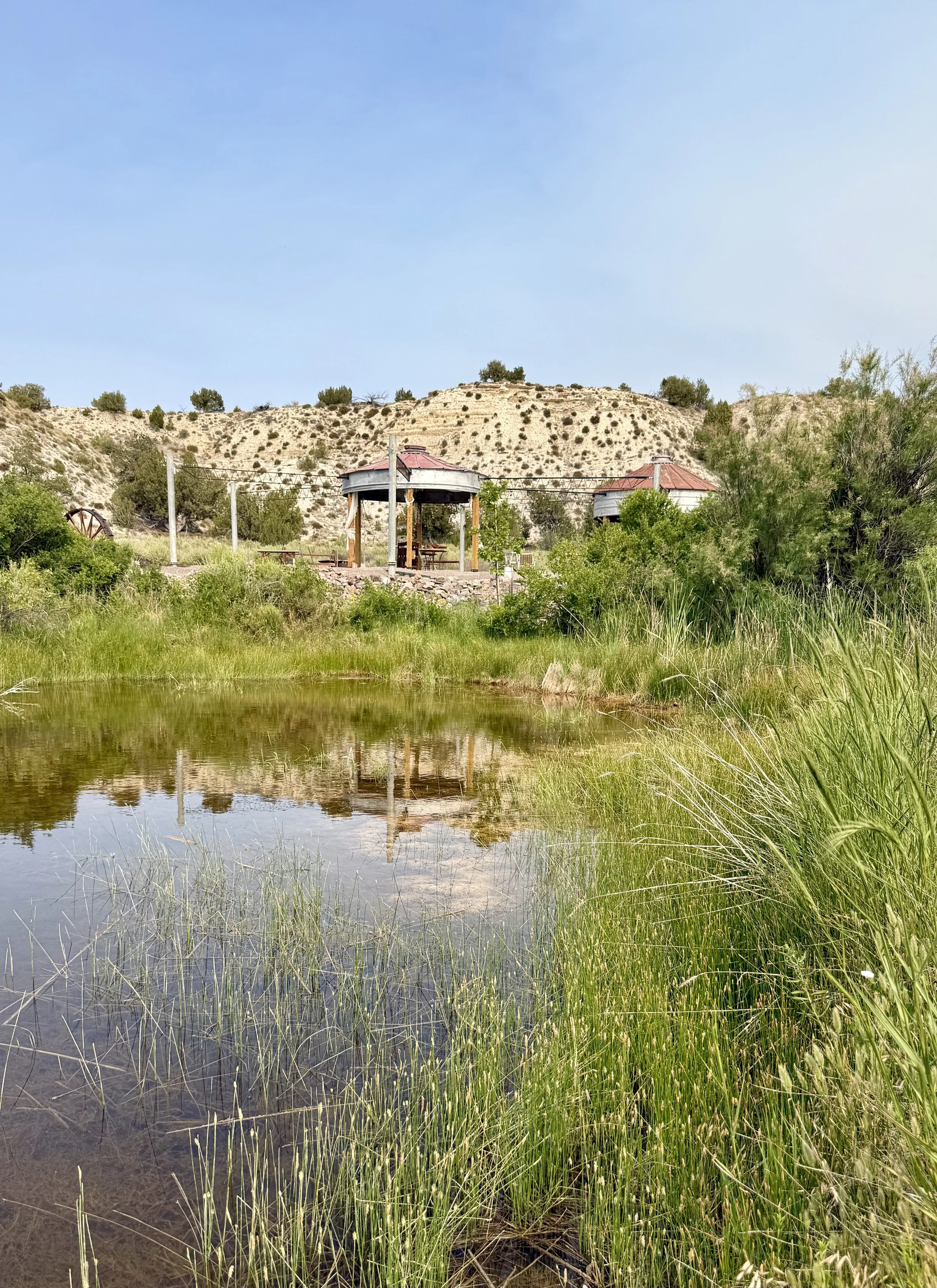 The wedding reception awning reflects in the pond along with the string lights at Lost Pond outdoor wedding venue near Pueblo, Colorado.