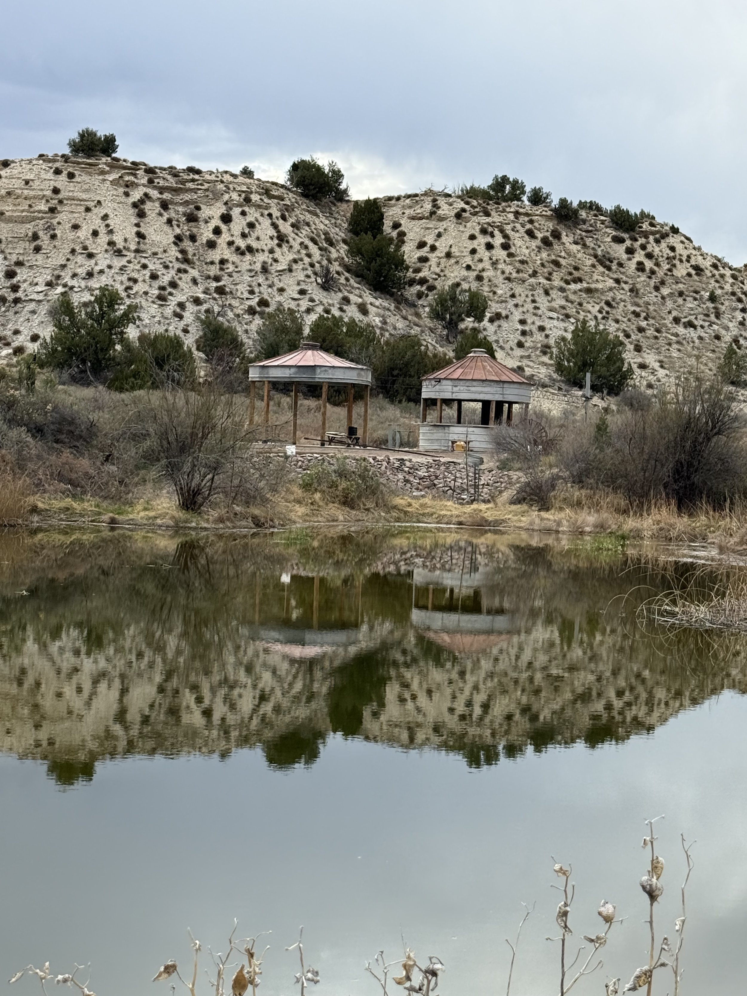 Grain bin silo dance floor gazebo and bar are reflected in the water at Lost Pond rustic outdoor wedding venue near Canon City, Colorado
