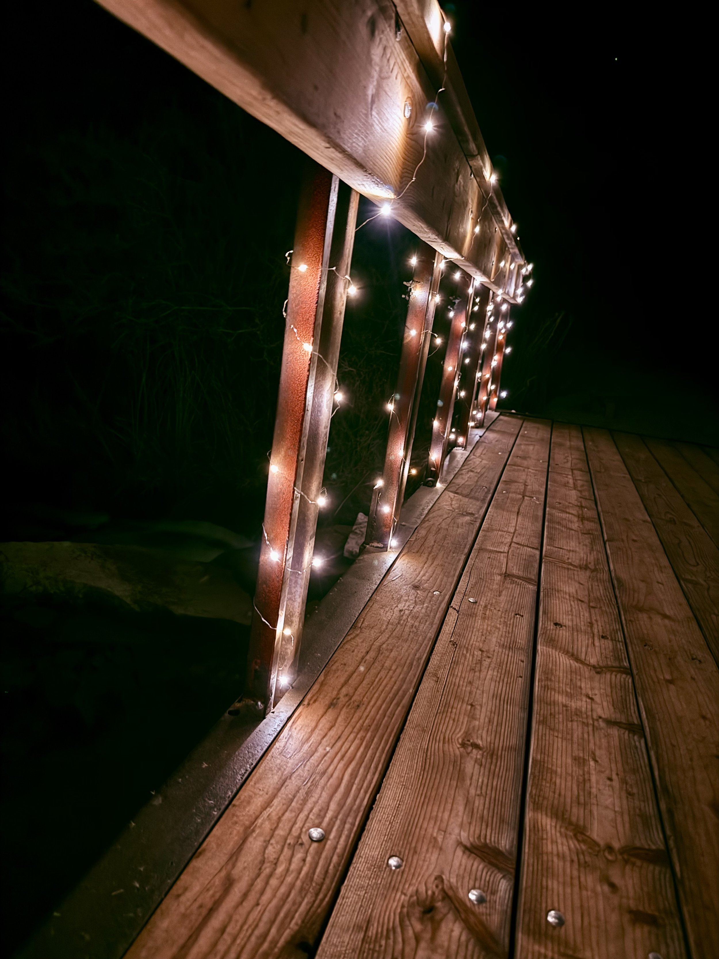 Bridge over the waterfall lit up with fairy twinkle lights at night at Lost Pond wedding venue near Canon City, Colorado