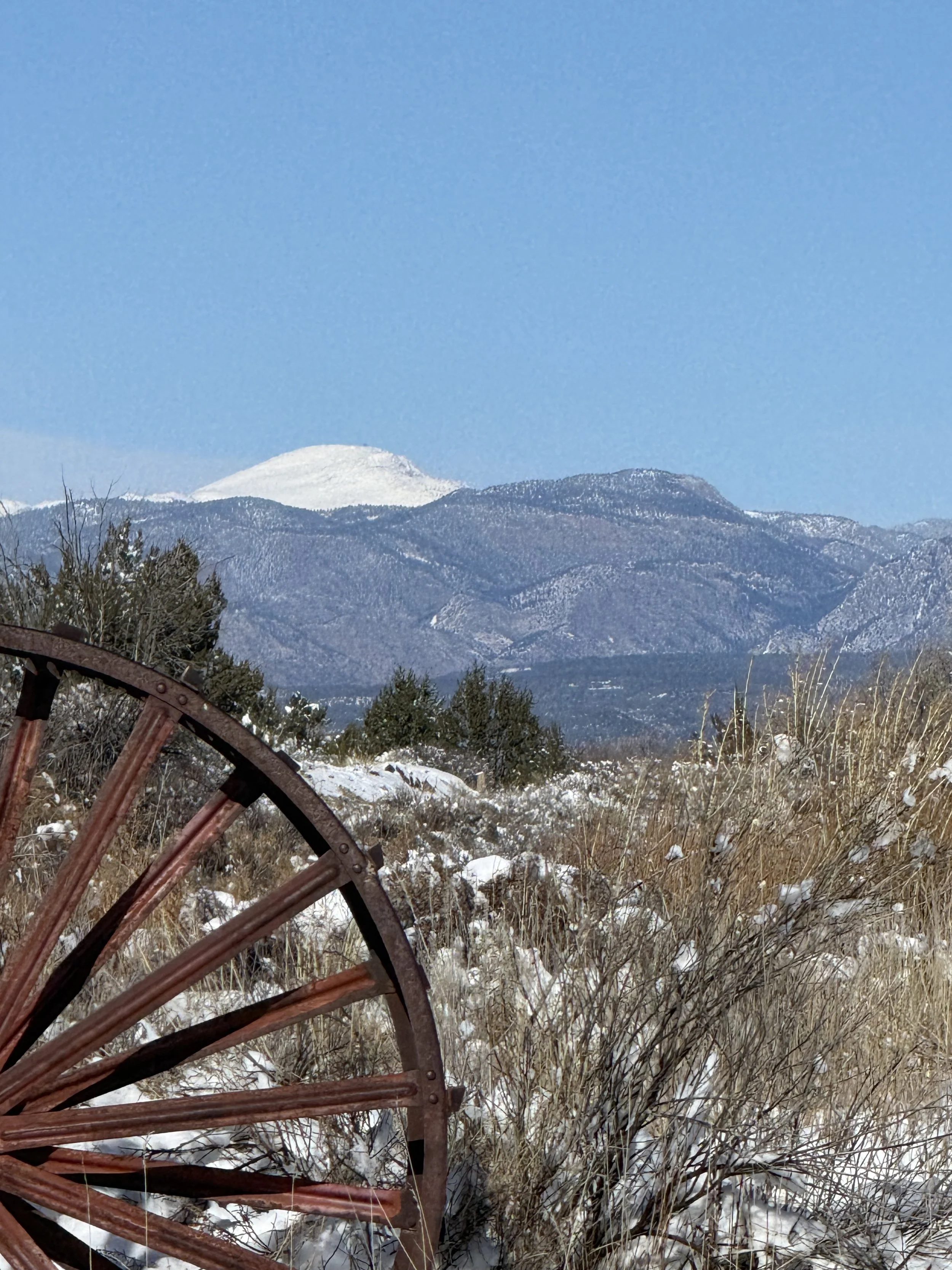 Pikes peak mountain view as rustic wagon wheel in the background as Pikes Peak towers over Colorado Springs and Lost Pond wedding venue.