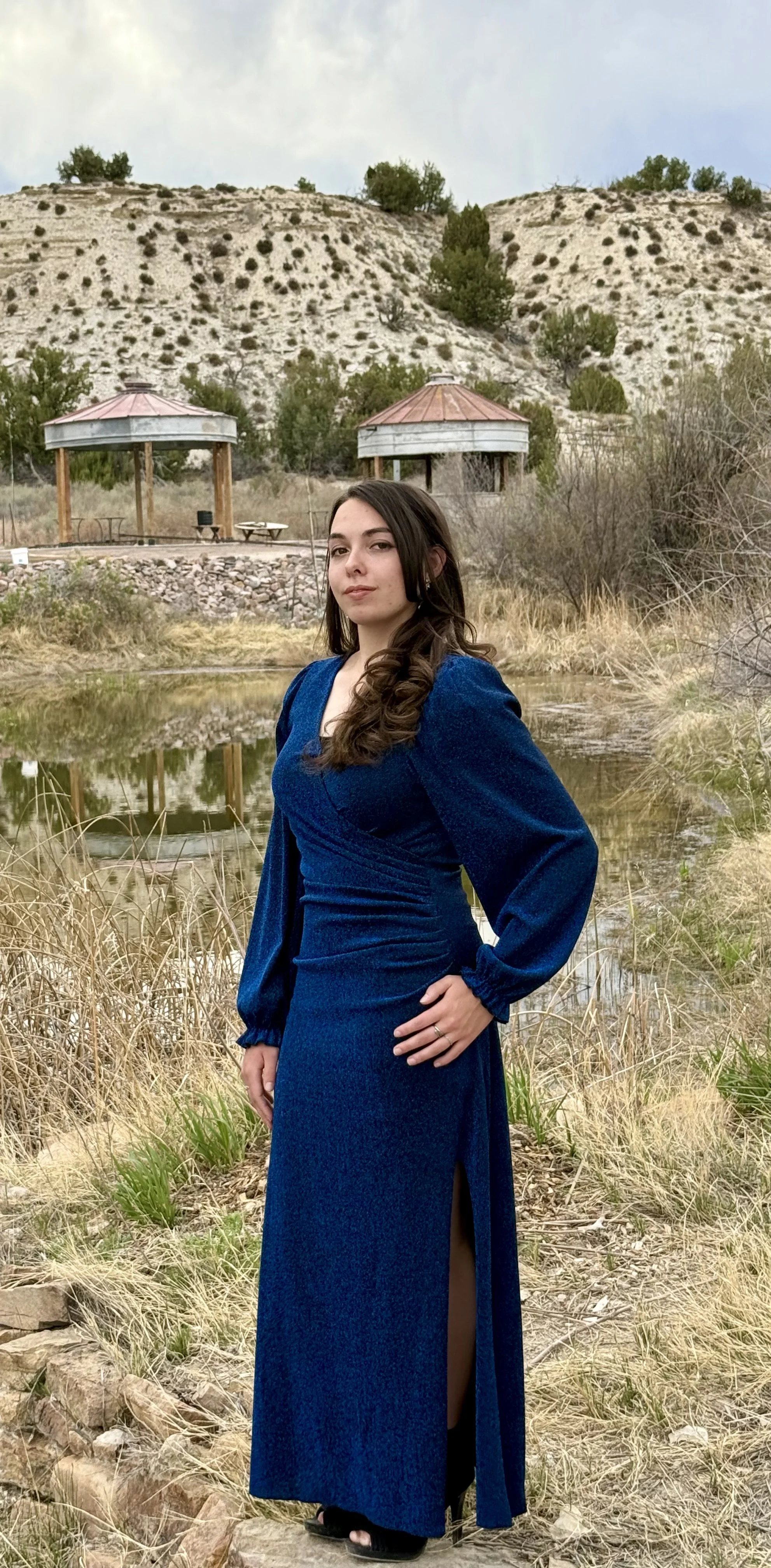 A bride standing next to the pond with a gazebo reflection in the water at waterside wedding venue Lost Pond, with a pond, lake, stream, river, waterfalls, and creek with a wooden bridge at Lost Pond wedding venue near Pueblo, Colorado.