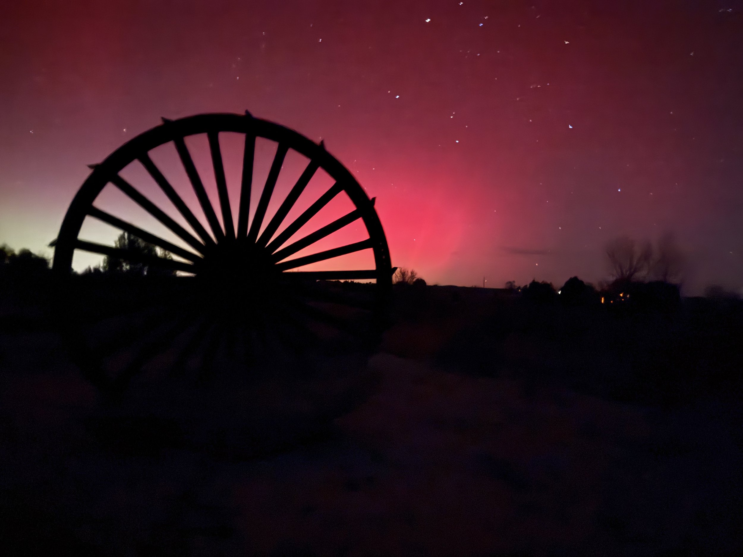 Northern Lights behind rustic wagon wheel with mountains behind at Lost Pond wedding venue near Canon City Colorado