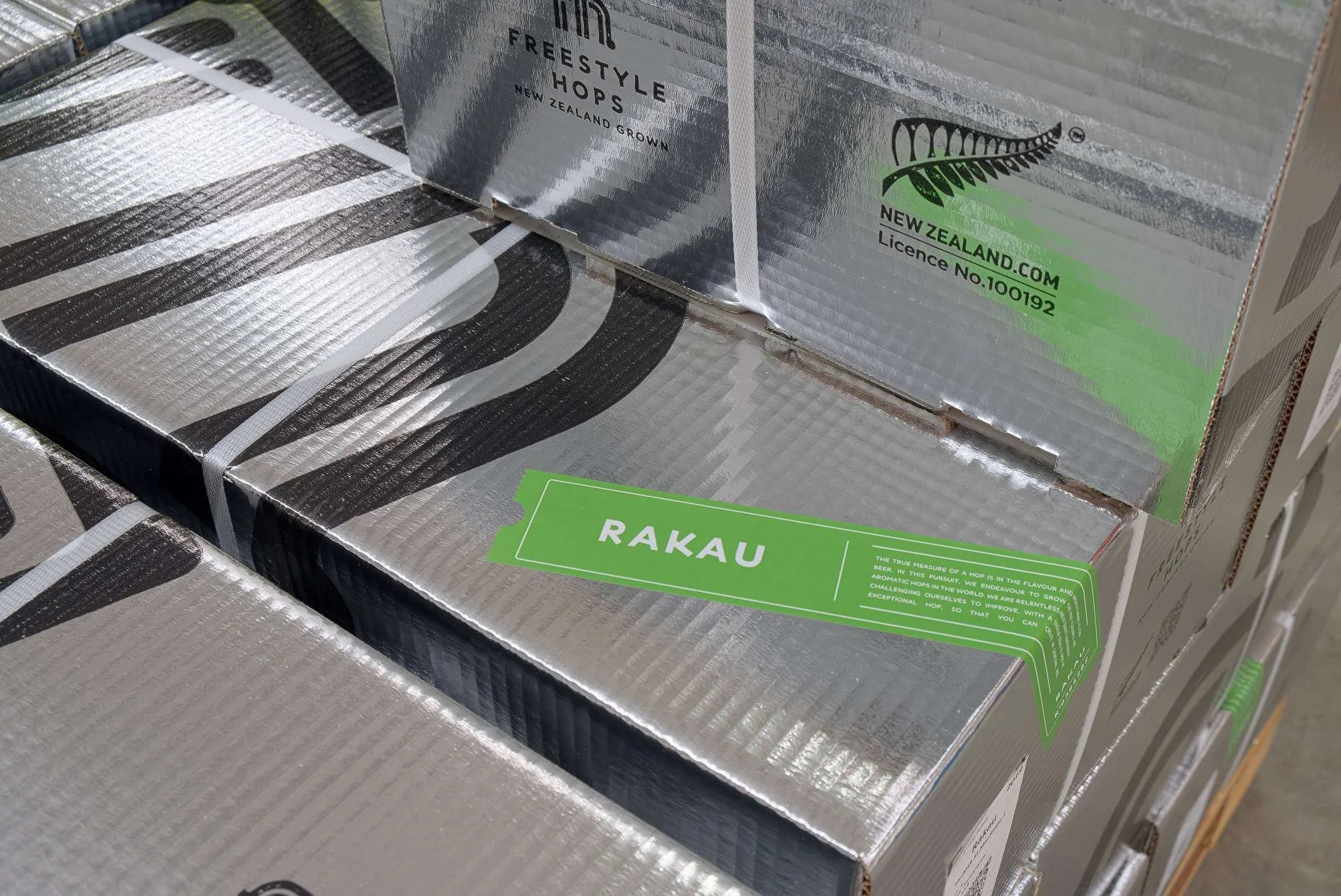 Stacked metallic silver boxes of Freestyle Hops beer with green labels reading 'RAKAU' and information about New Zealand grown hops.