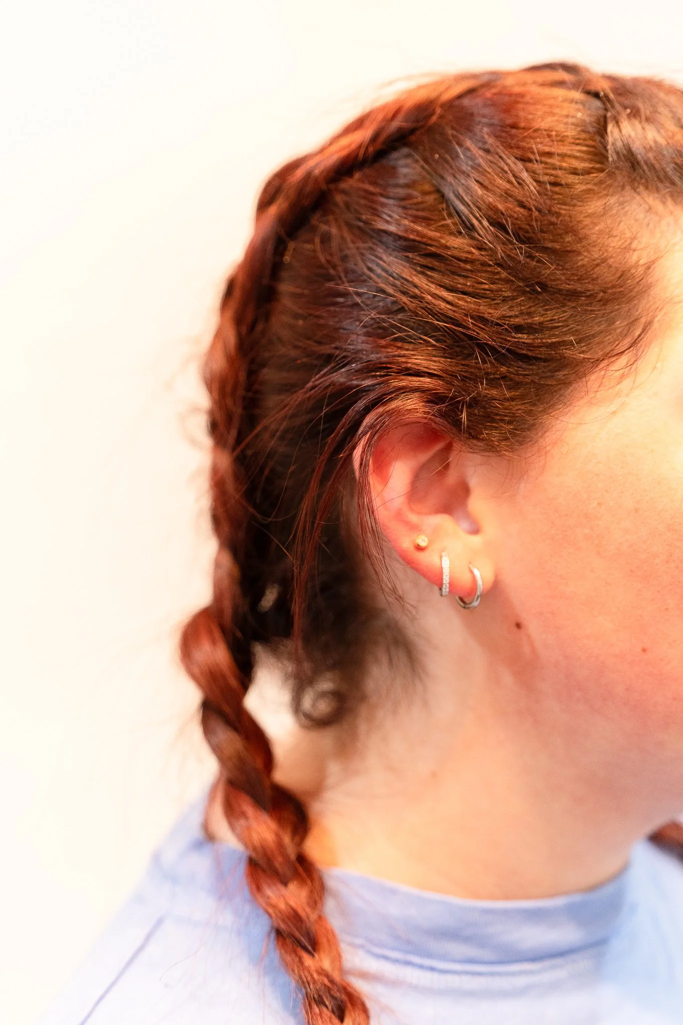 Close-up of a teenager's head showcasing red braided hair and her new pediatric ear piercing.