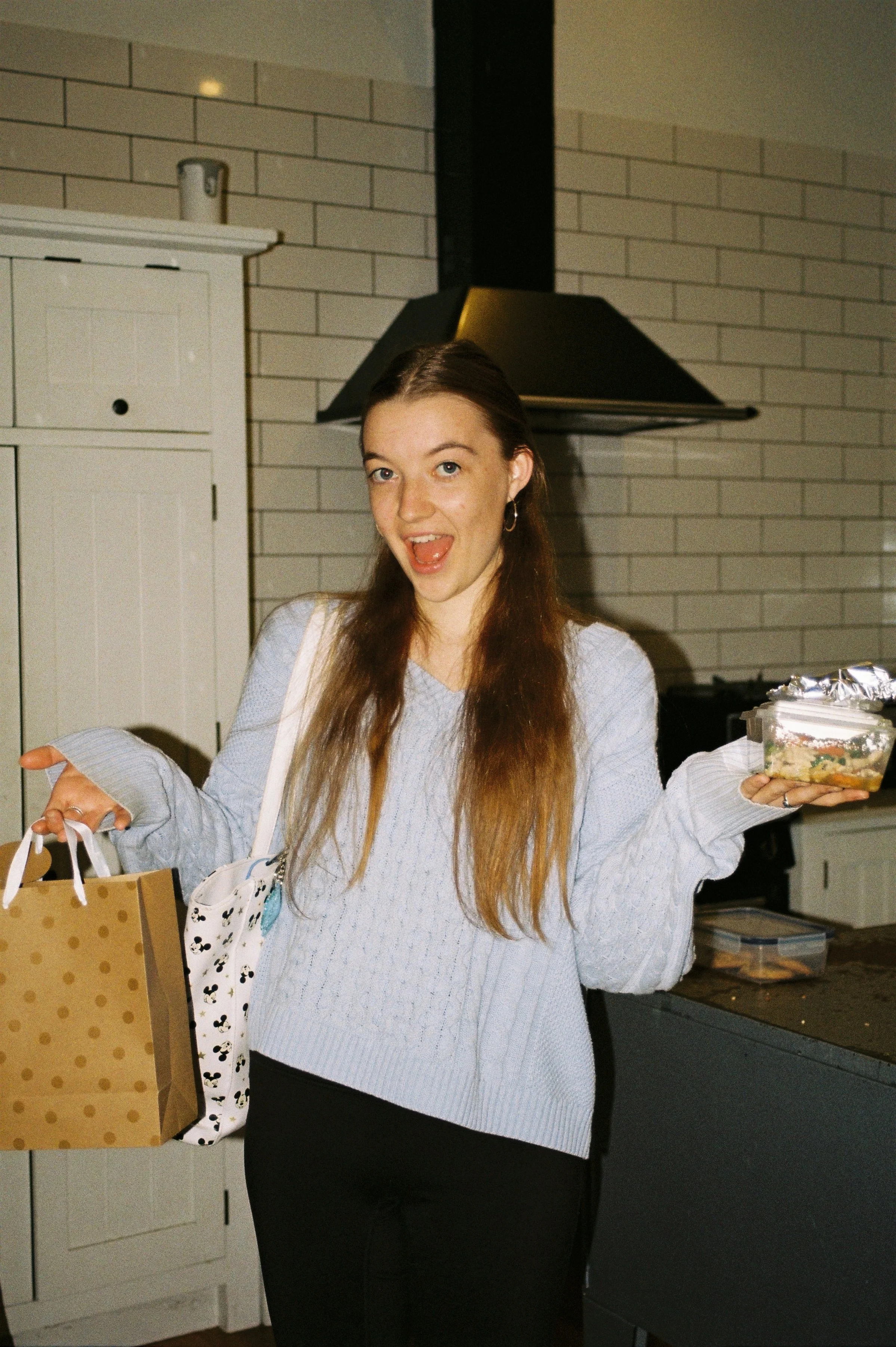 A young woman smiling whilst holding many bags and items.