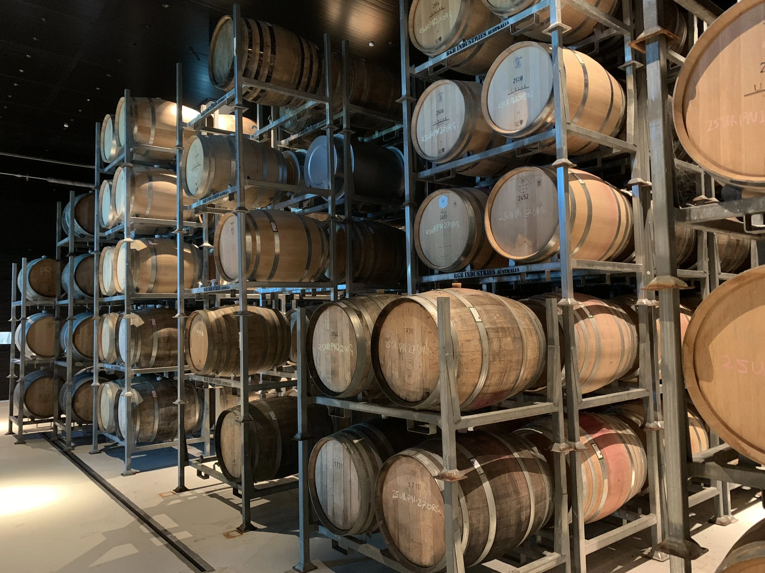 Multiple wooden wine barrels stored on metal racks in a storage room or cellar.