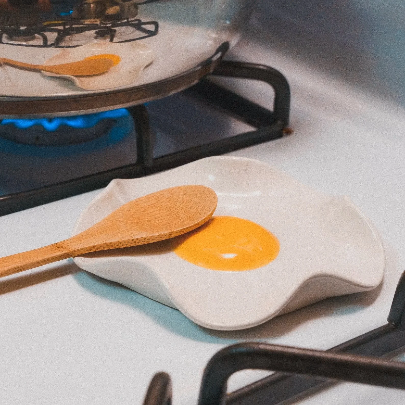 Hand-sculpted ceramic spoon rest shaped like a fried egg, perfect for sunny-side-up enthusiasts and playful countertop decor.