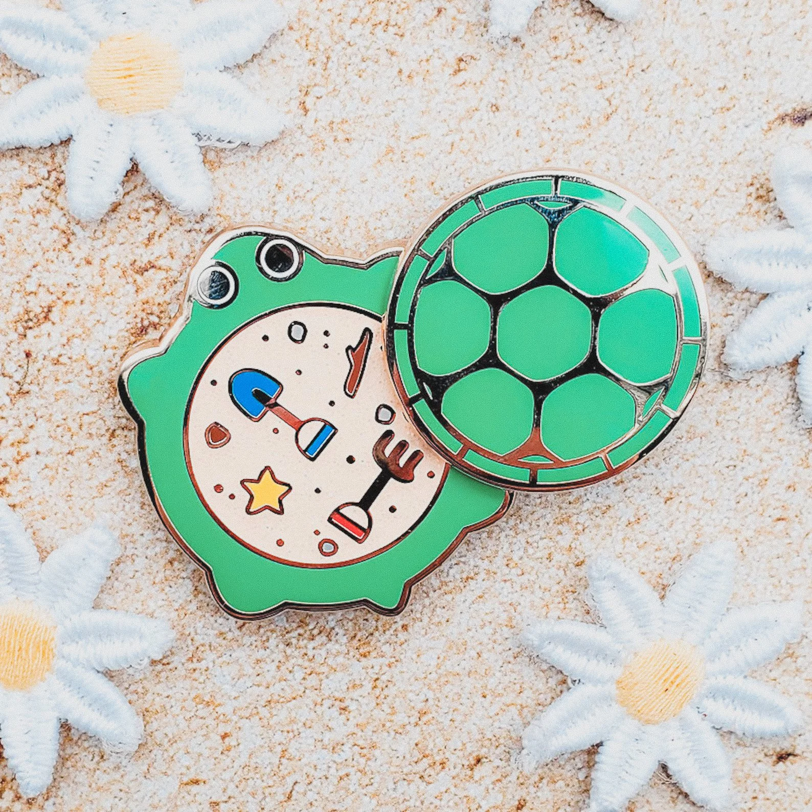 Playful enamel pin featuring a turtle sandbox with swivel lid, great for nostalgic 90s kids, pin collectors, or playful bag flair.
