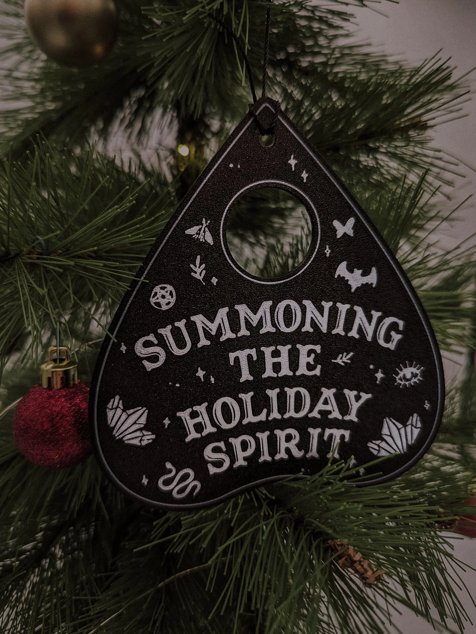 Black Christmas ornament with ghostly white lettering that reads “Summoning the Holiday Spirit,” perfect for gothmas trees and spooky seasonal décor.