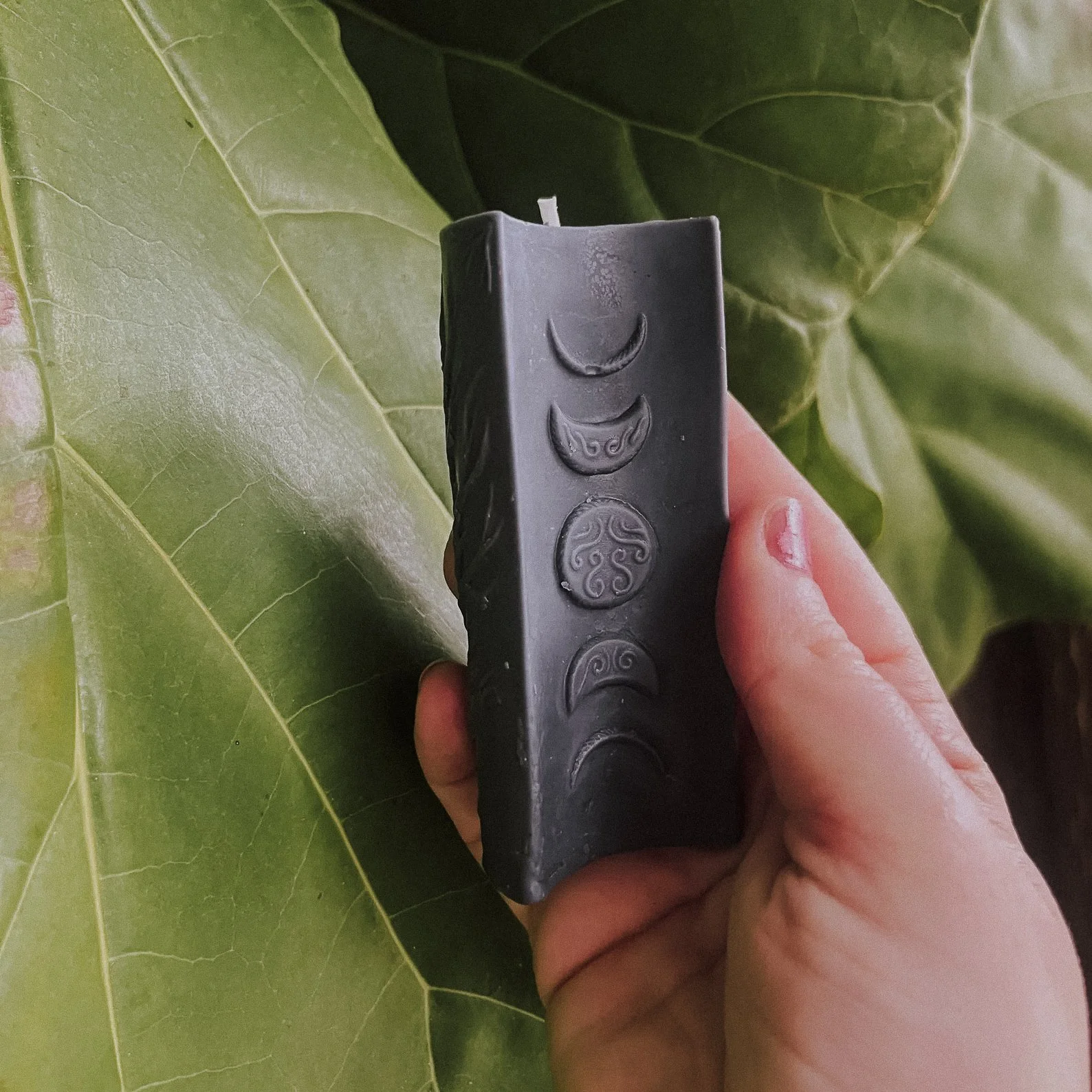 A 4x2.7-inch unscented white beeswax pillar candle featuring intricate carvings of moon phases, a bare tree, and spiral designs on its three sides. This astrology-inspired candle serves as both a decorative piece and a tool for lunar rituals, radiati