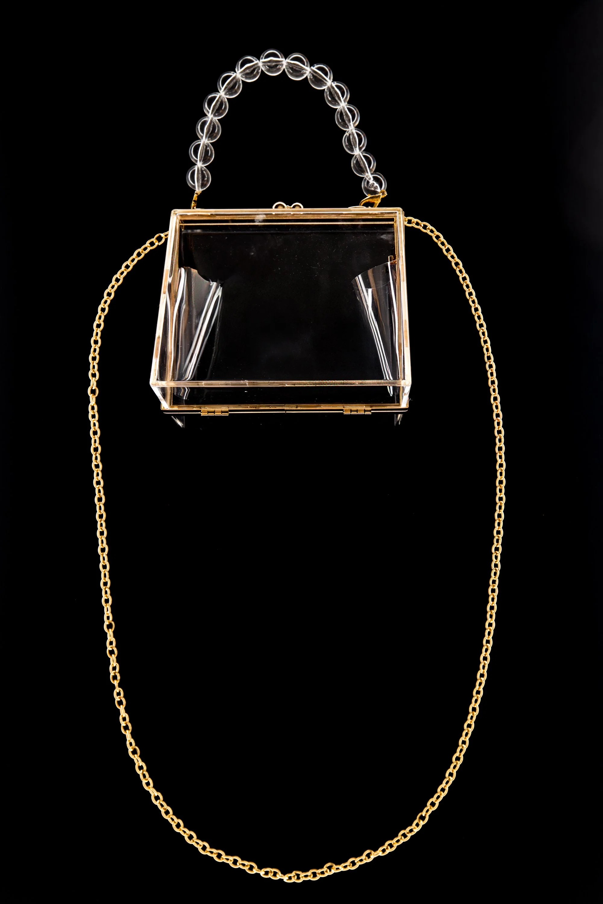 A transparent handbag with gold chain strap, adorned with a clear beaded handle.