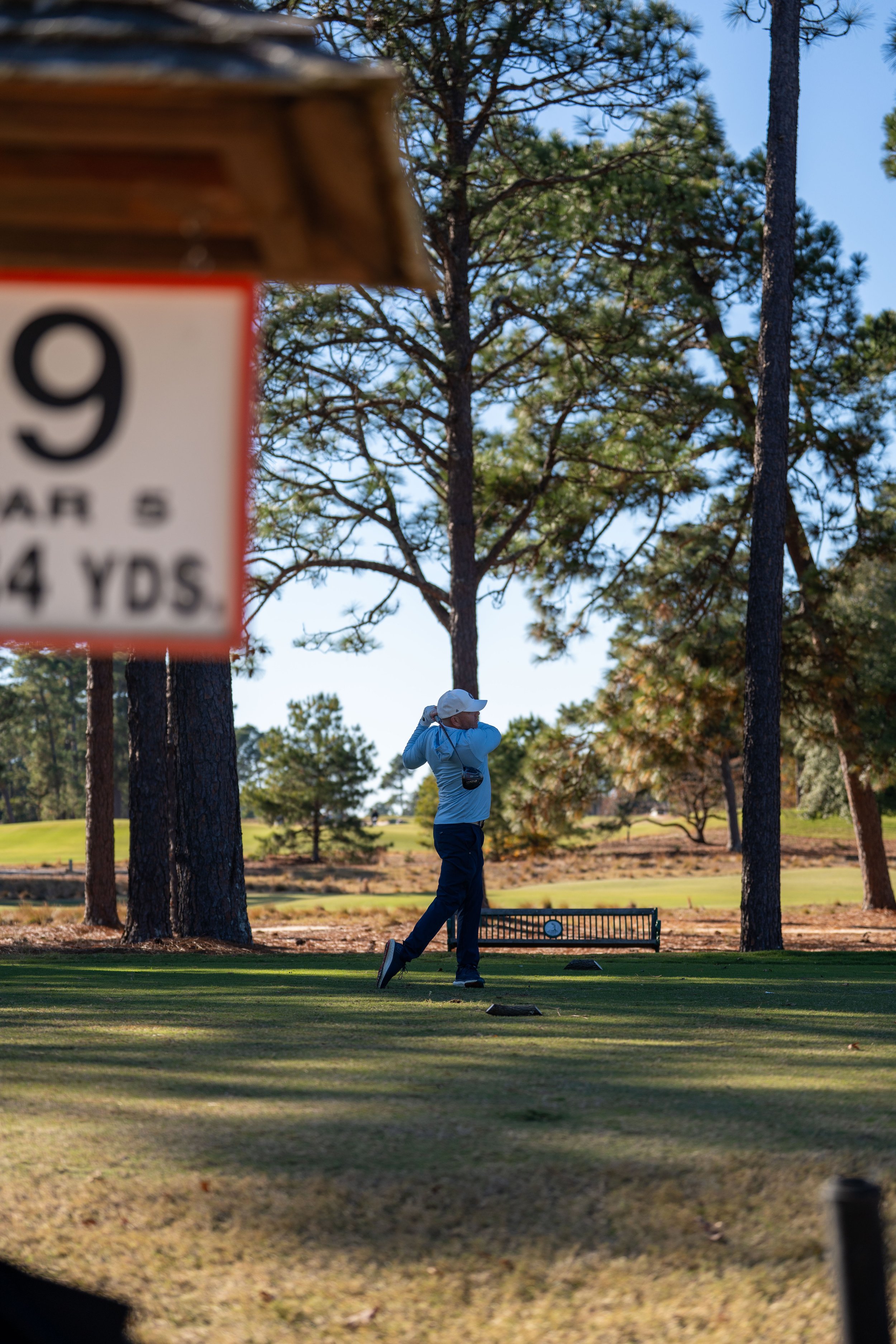 A person playing golf on a sunny golf course surrounded by trees, swinging a golf club.