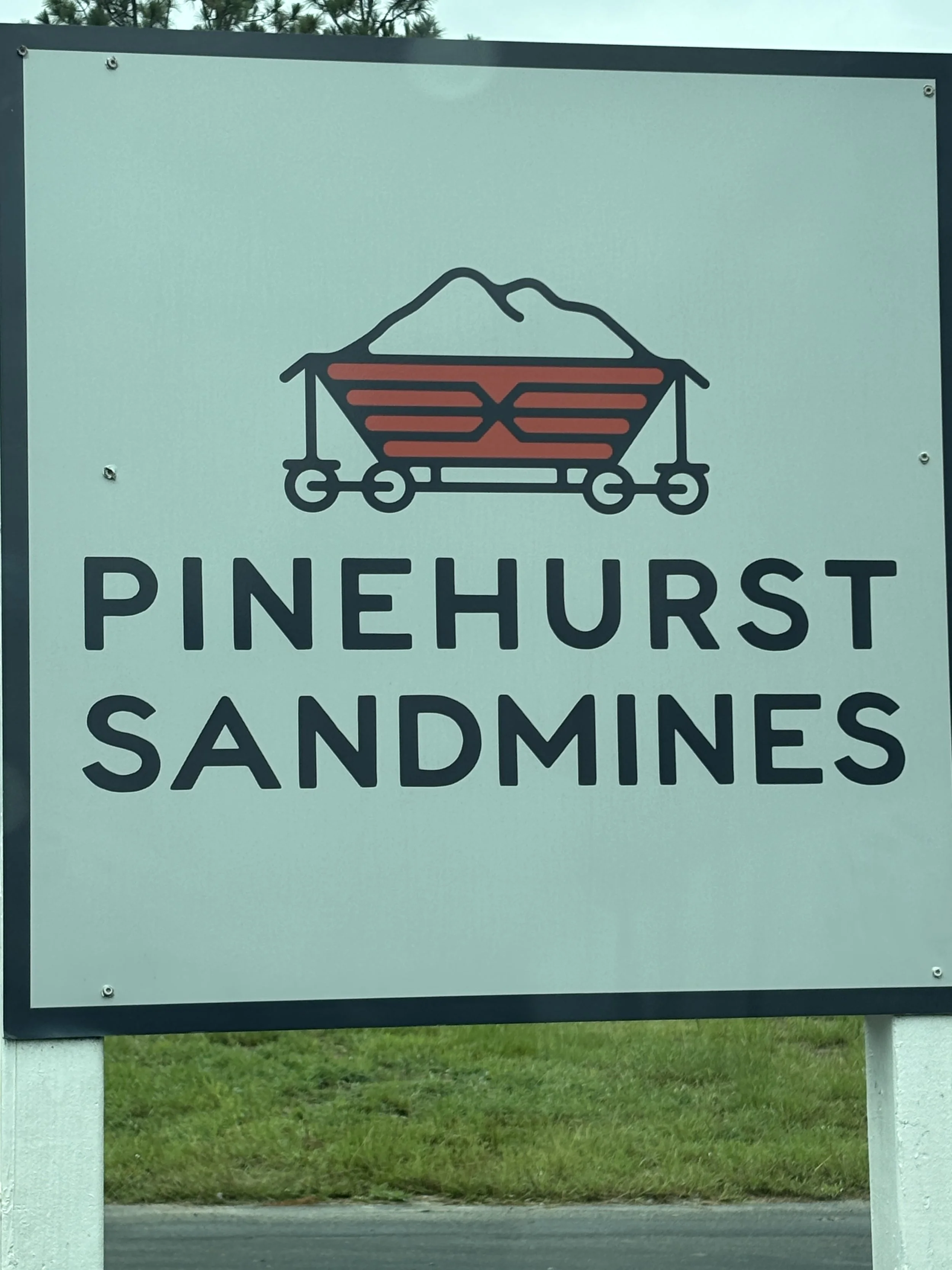 Sign for Pinehurst Sandmines featuring a mountain and sandcart graphic.