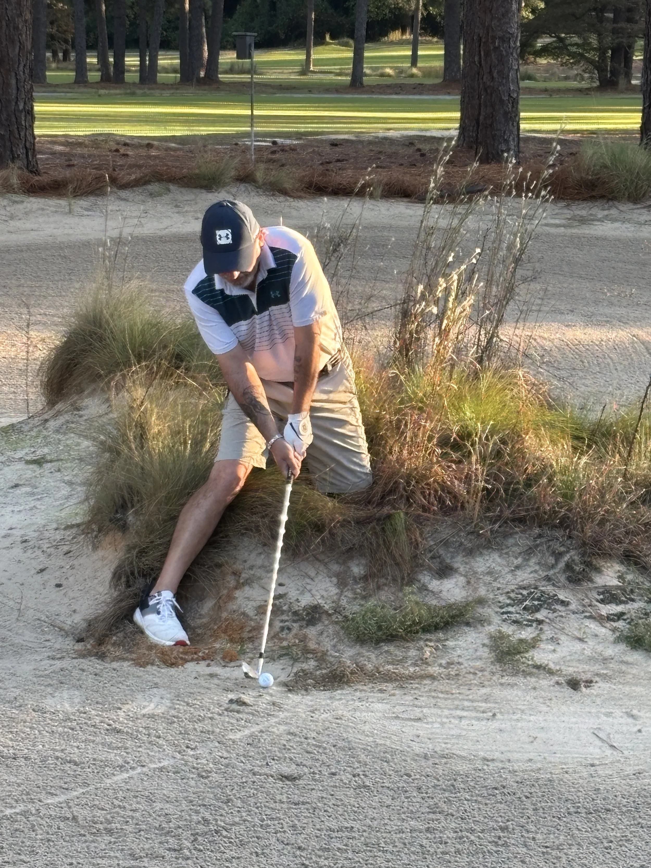 Man hitting a golf ball out of a sand trap on a golf course during sunset.