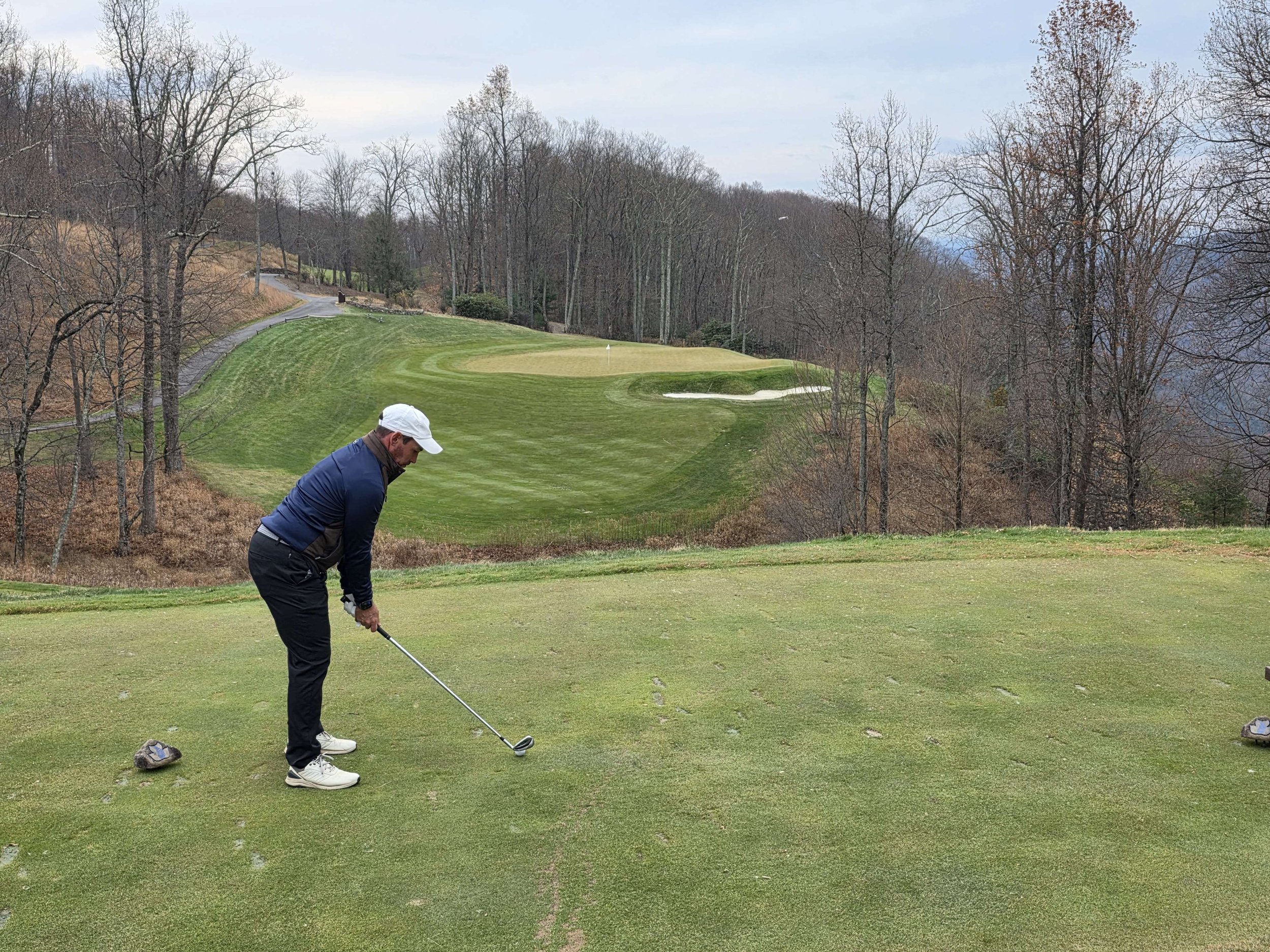 A man playing golf on a course with a green, sand traps, and trees in the background.