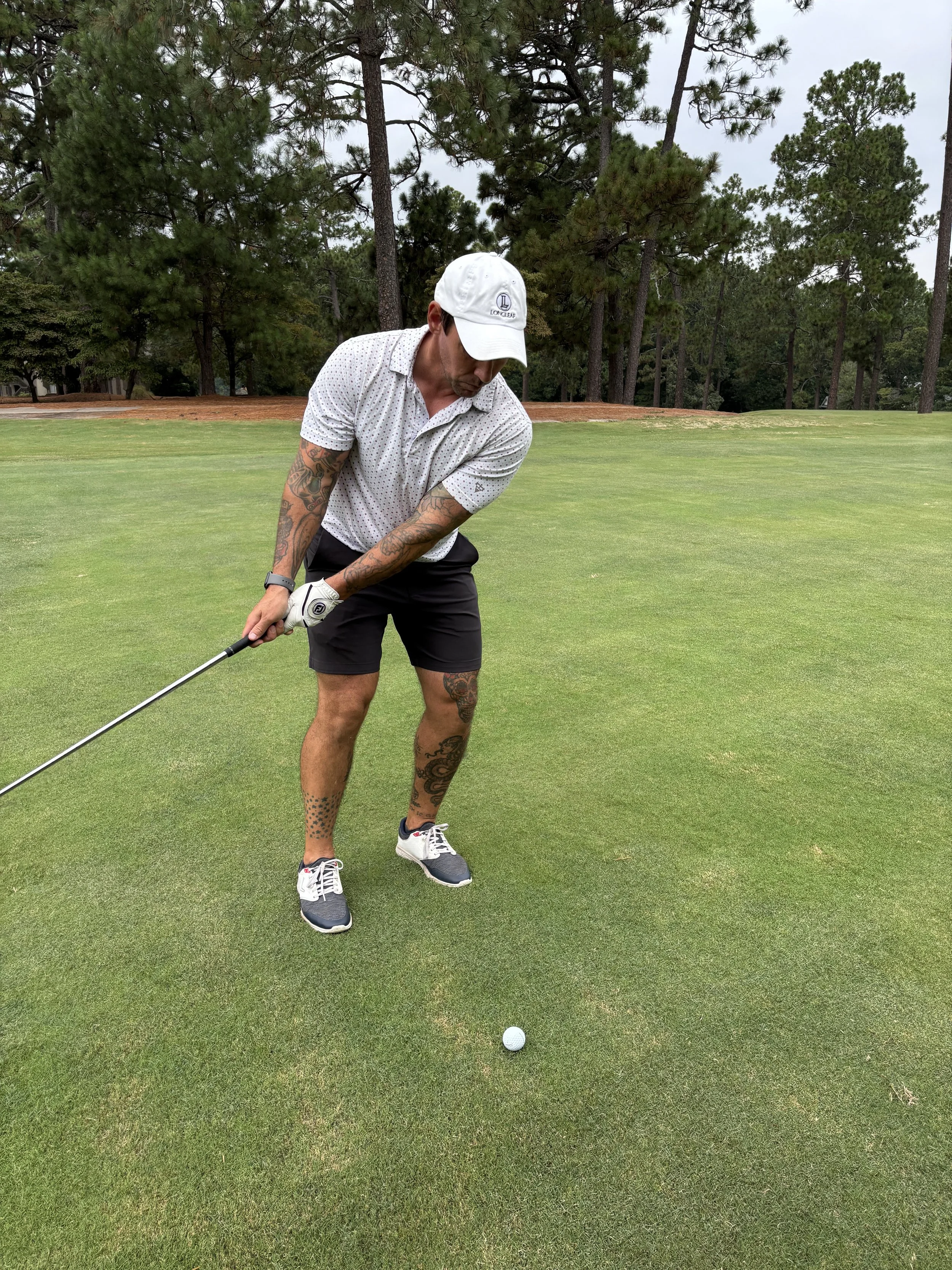 A man standing on a golf course preparing to hit a golf ball with a club, surrounded by trees and grass.