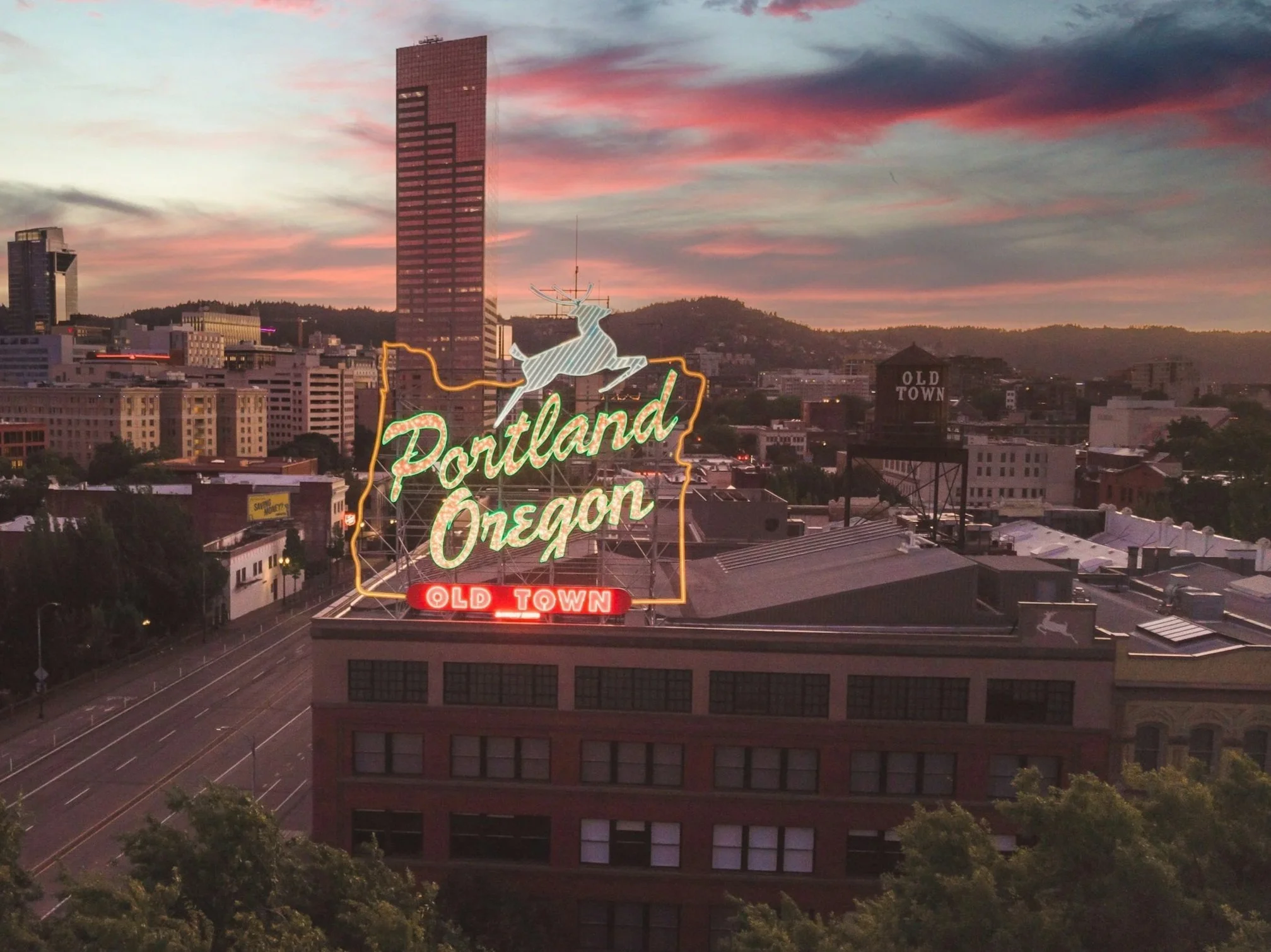 Cityscape of Portland, Oregon at sunset with a neon sign reading 'Portland Oregon Old Town' featuring a reindeer.