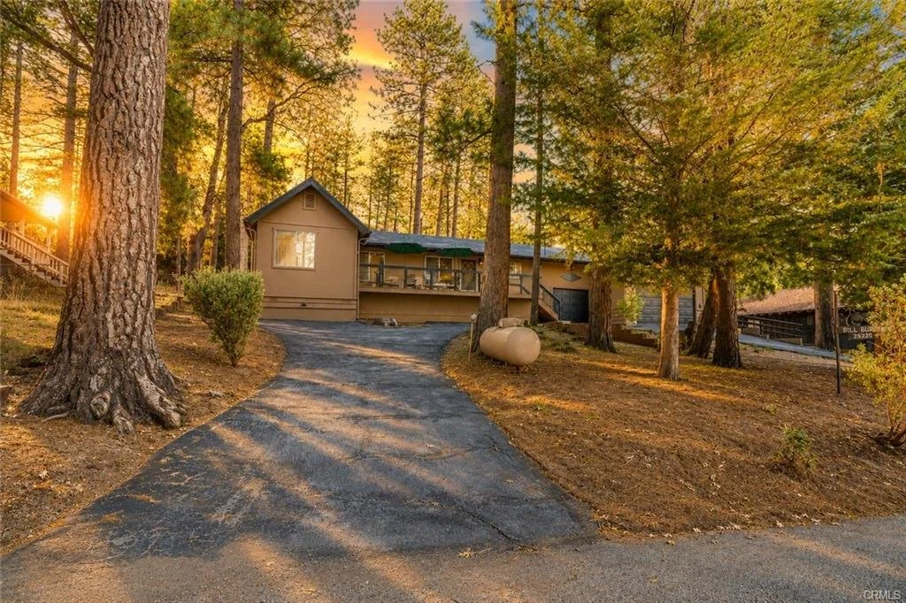 A house in the woods at sunset with a driveway leading up to it.