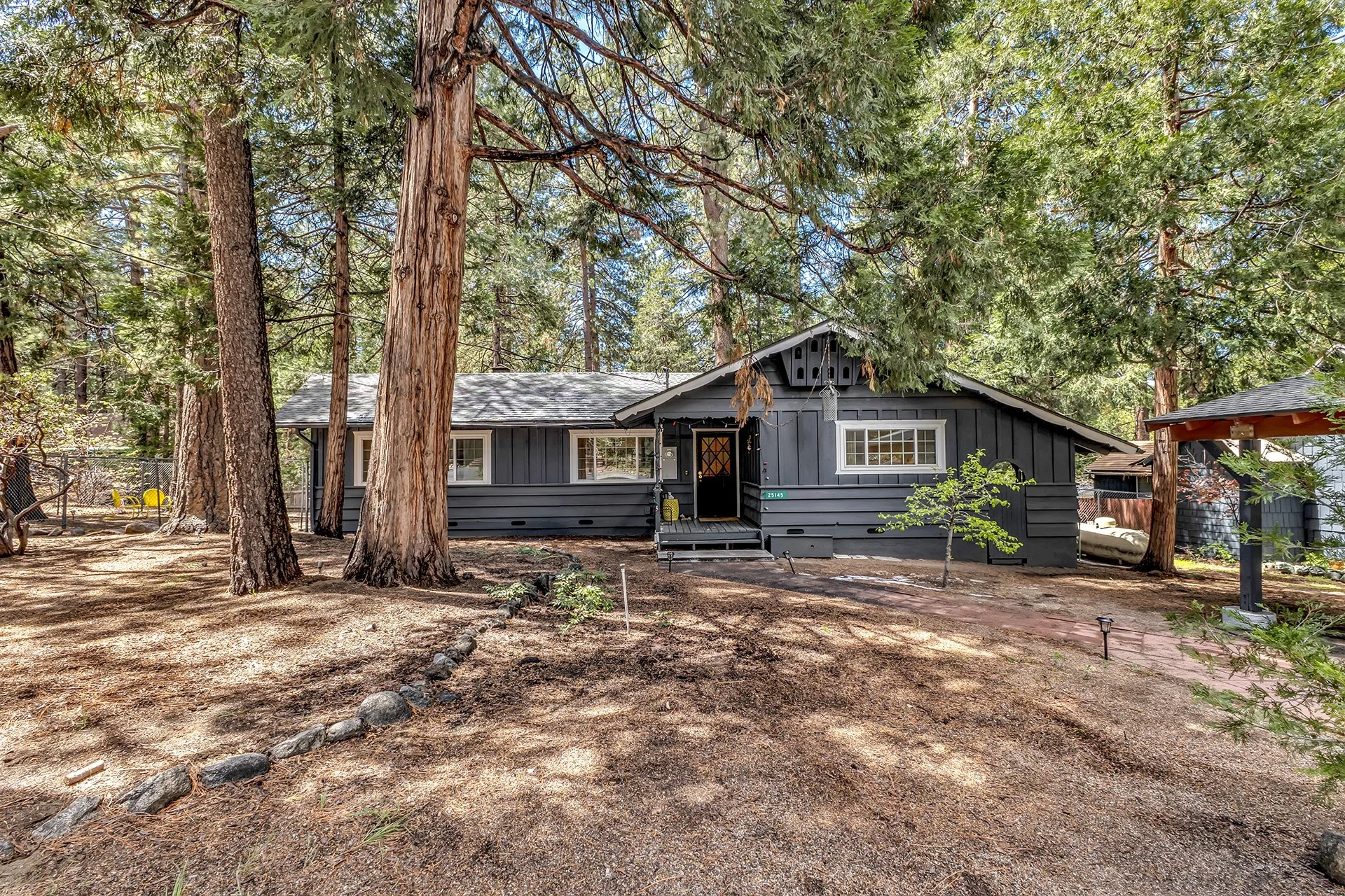 A gray house in a wooded area with tall trees surrounding it, a small front porch, and a pathway leading up to the entrance.