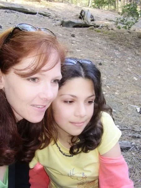 A woman and girl taking a selfie outdoors in a wooded area.